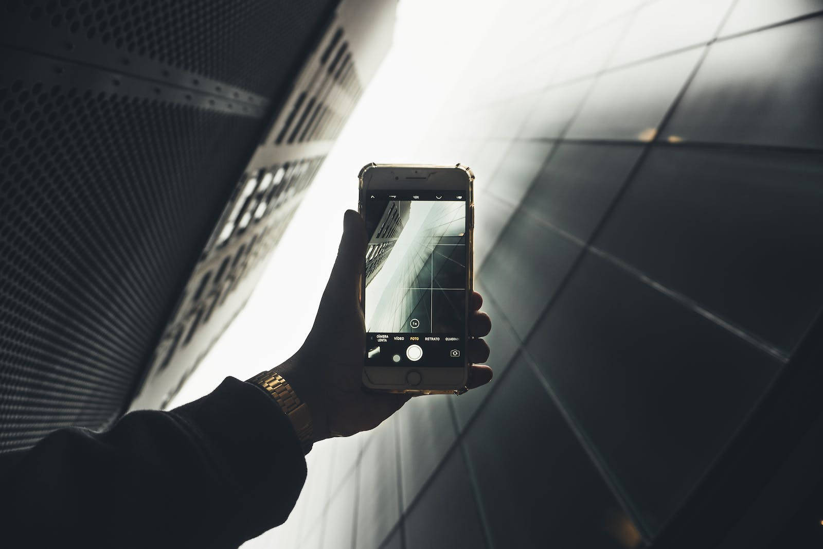 original iPhone 6 桌布 壁紙 — 一隻手握住智慧型手機，以低角度拍攝現代建築的幾何立面，帶有戲劇性的背光。