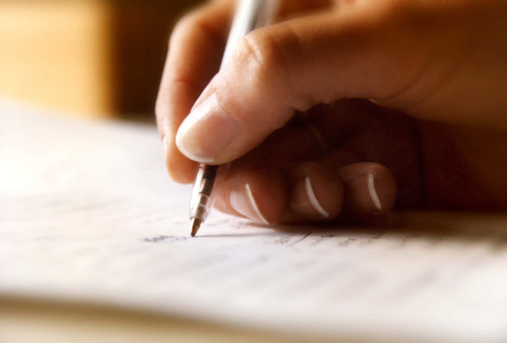 Writing 桌布 壁紙 — 一隻手握住筆在紙上書寫的特寫，光線柔和溫暖。