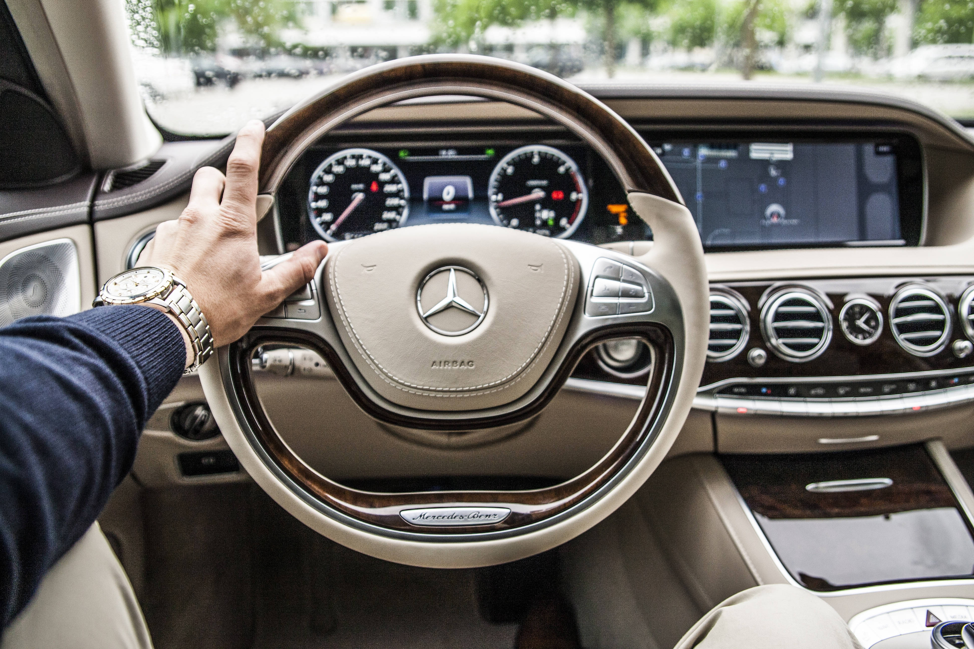 Mercedes 桌布 壁紙 — 一隻手握著賓士S-Class的豪華方向盤，展示其高級米色皮革和木紋飾板內裝。