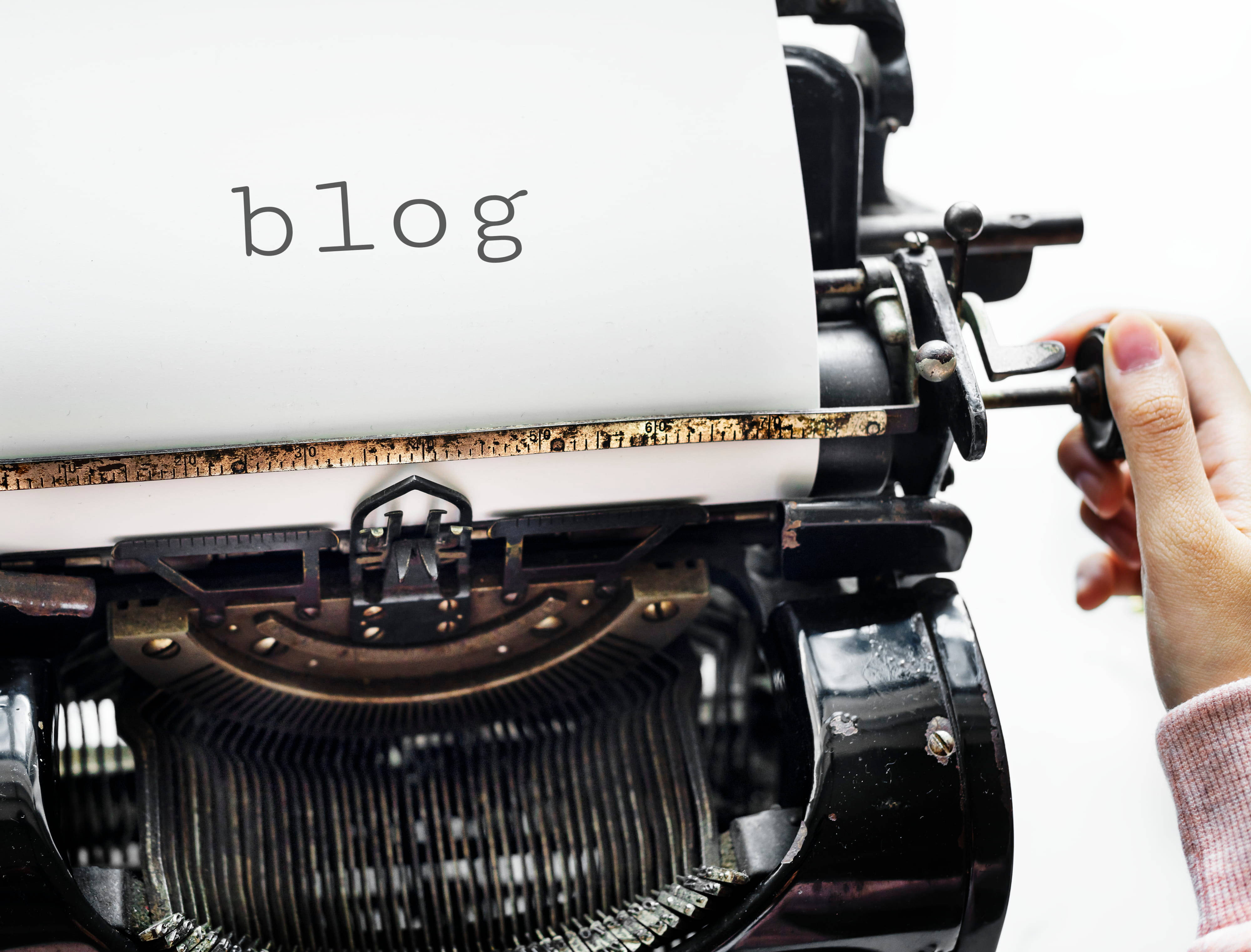 白色 桌布 壁紙 — 一隻手正在調整一台復古打字機，紙上打著「blog」這個詞，背景是純白色。