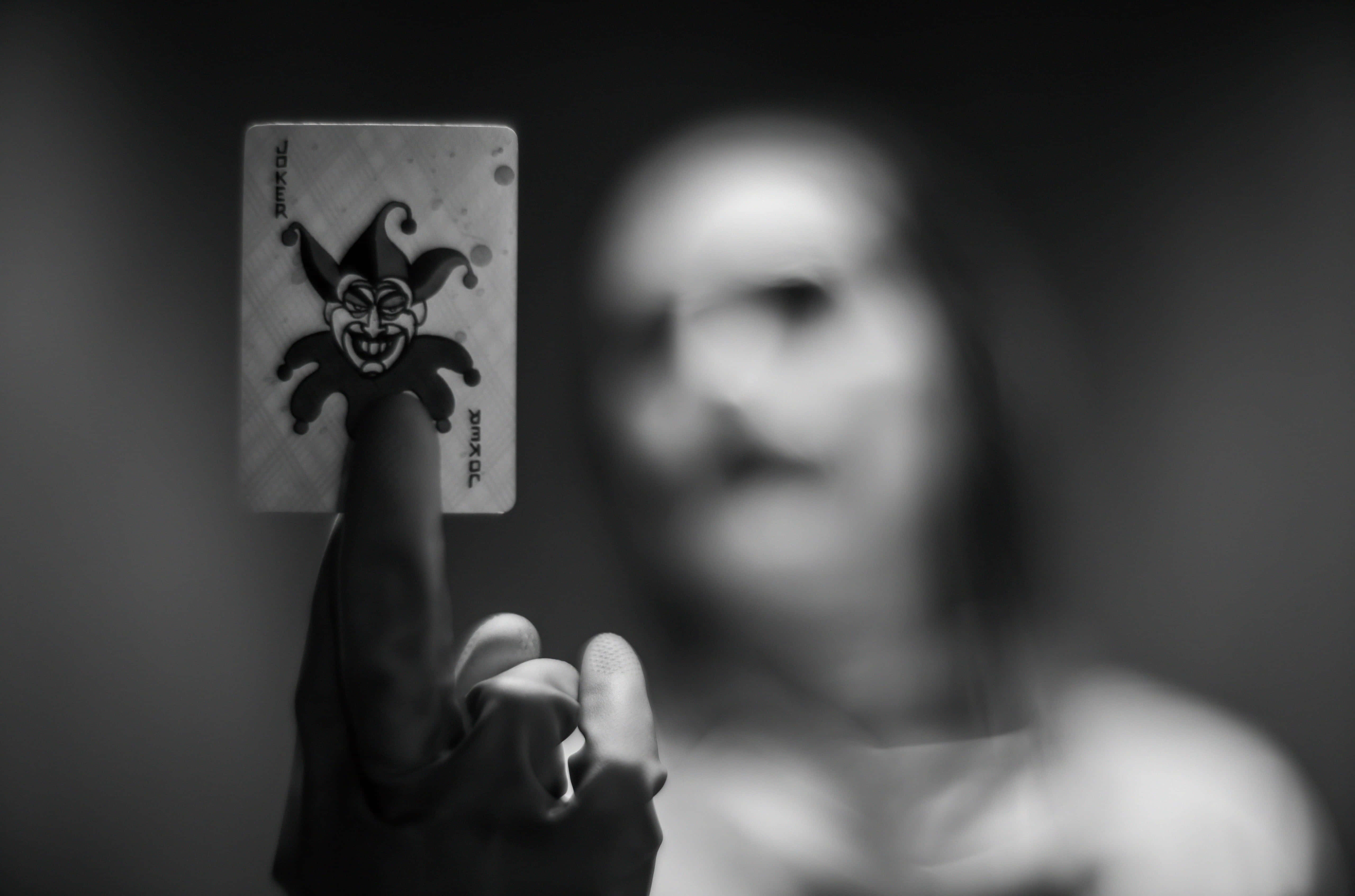 Joker Card 桌布 壁紙 — 一隻手清晰對焦地拿著一張小丑撲克牌，而一個模糊的人影在背後以單色呈現。