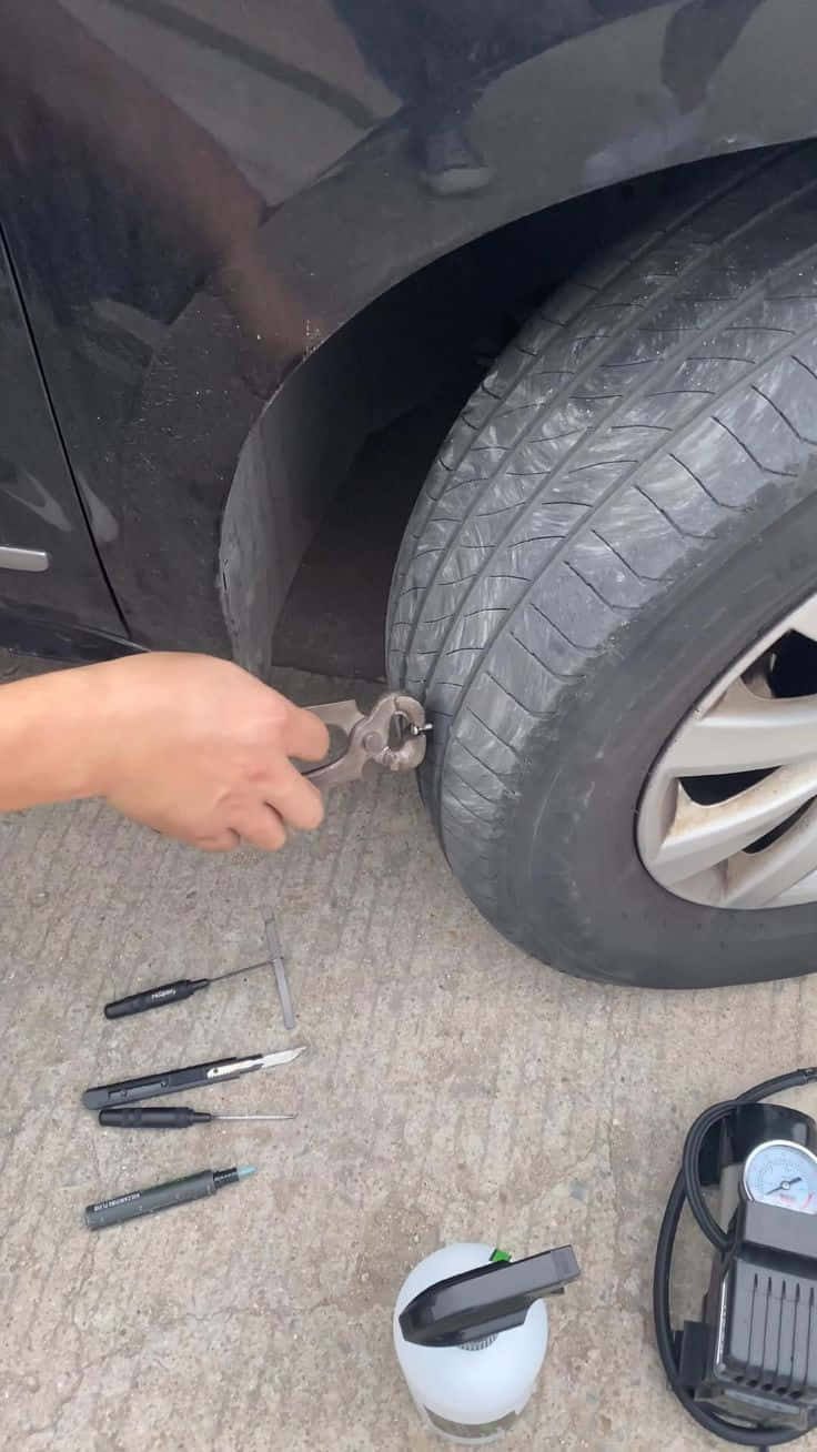 Flat Tire 桌布 壁紙 — 一隻手用十字扳手收緊黑色汽車輪胎上的輪胎螺母，工具散落在混凝土地面上。