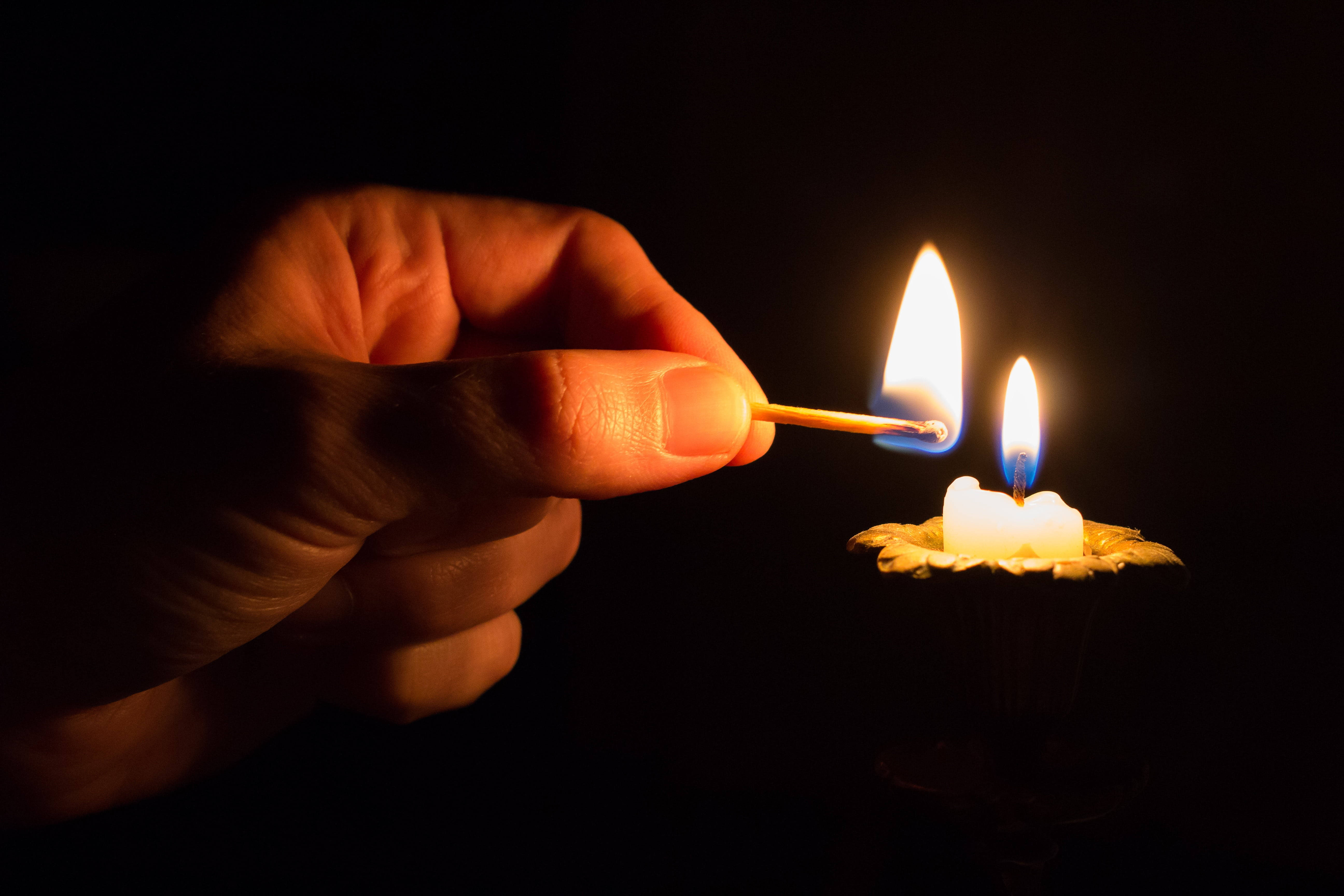 蠟燭 桌布 壁紙 — 一隻手用火柴點燃蠟燭，在純黑背景下投射出溫暖的金色光芒。