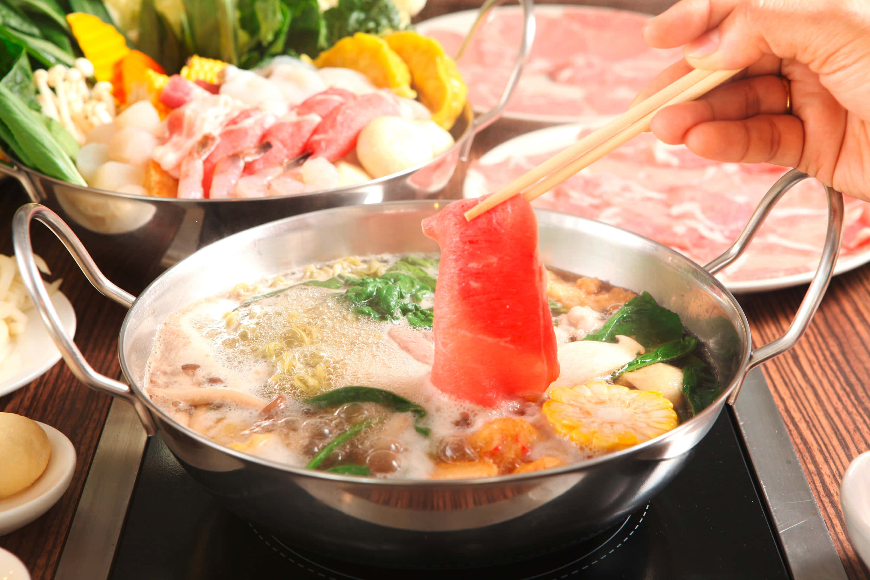 meat 桌布 壁紙 — 一隻手用筷子將一片生牛肉蘸入一個冒著熱氣、有湯底、蔬菜和麵條的火鍋中。