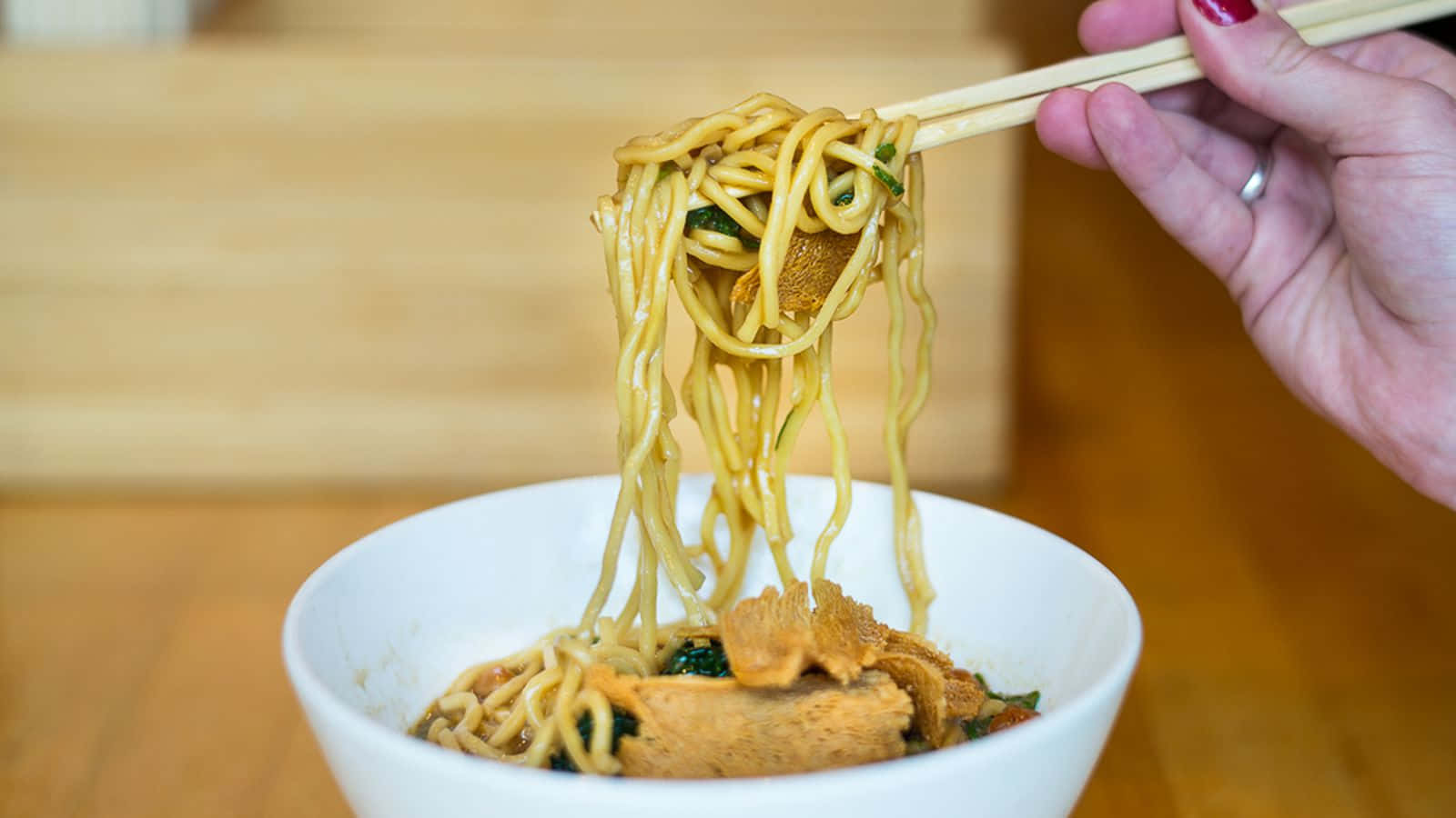 Noodles 桌布 壁紙 — 一隻手用筷子從裝滿濃郁湯頭和豆腐的白色碗中夾起冒著熱氣的麵條。