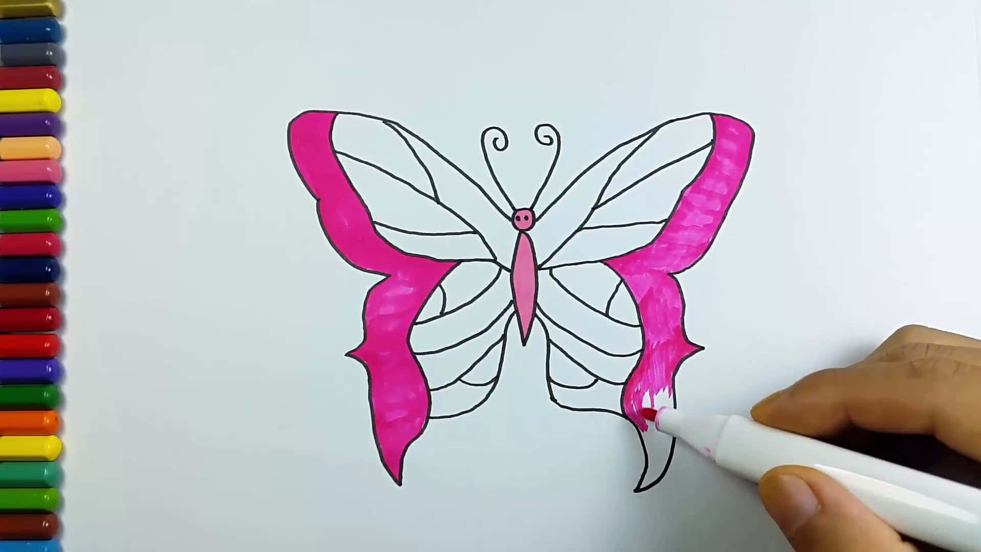 Butterfly Coloring Pages 桌布 壁紙 — 一隻手用粉紅色麥克筆在白色紙上為蝴蝶輪廓上色，旁邊有一排彩色麥克筆。