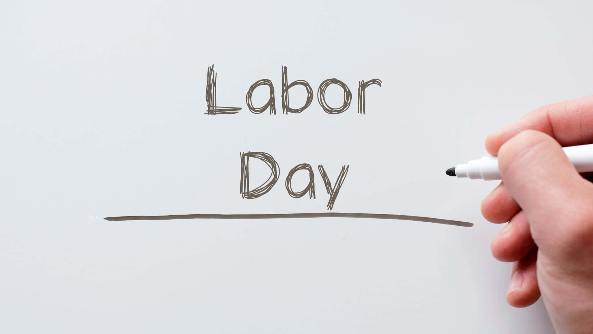 勞動節 桌布 壁紙 — 一隻手用粗頭記號筆在乾淨的白色表面上寫下「Labor Day」，並整齊地畫上底線。