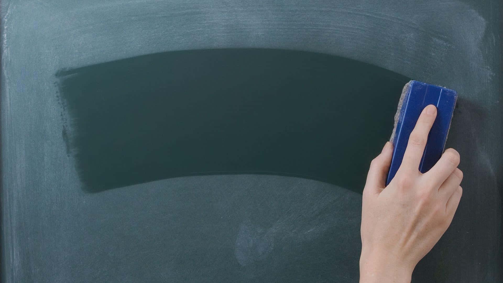 Blackboard 桌布 壁紙 — 一隻手用藍色橡皮擦擦去彎曲的深綠色黑板上的粉筆痕跡。