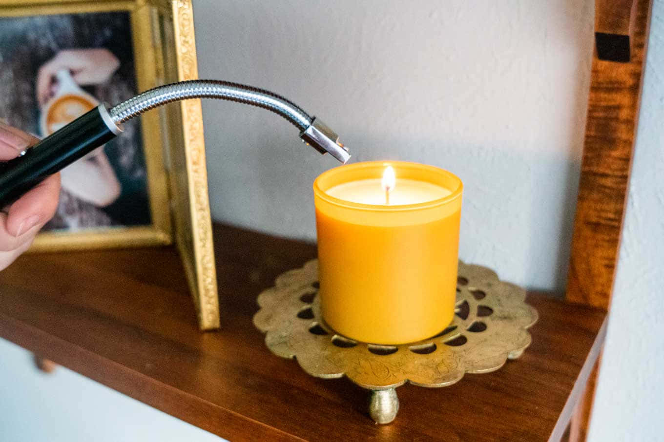 lighter 桌布 壁紙 — 一隻手用金屬火炬點燃一個發光的黃色蠟燭，放在一個華麗的黃銅杯墊上，旁邊是一個帶框的照片。