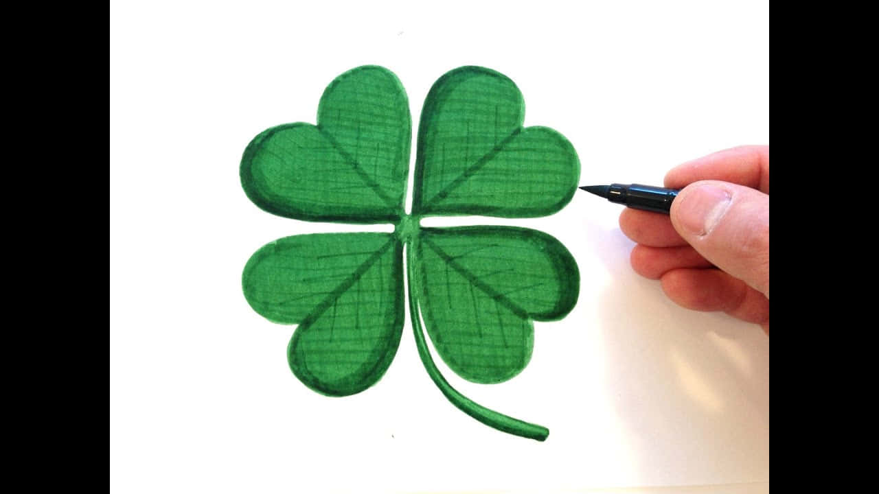 Four Leaf Clover 桌布 壁紙 — 一隻手用黑色筆在白色紙上以交叉陰影畫法畫出充滿活力的綠色四葉草。