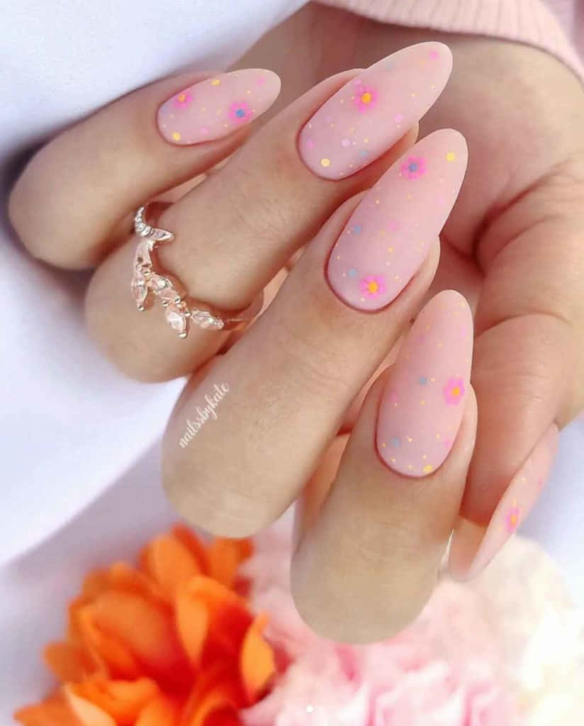 Nail Art 桌布 壁紙 — 一隻手的特寫，帶有粉彩粉紅色指甲，飾有細小彩色花朵和亮粉，旁邊放著柔和的橙色和粉紅色花朵。