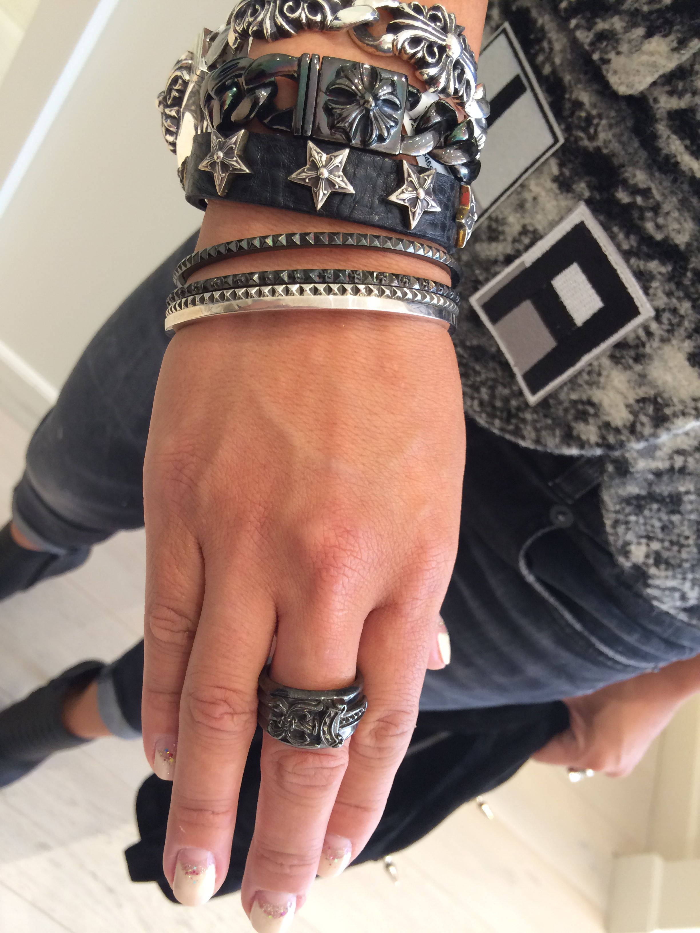 Chrome Hearts 桌布 壁紙 — 一隻手的特寫，戴著多條銀色星星手鍊和一個華麗戒指，襯著一件圖案襯衫。