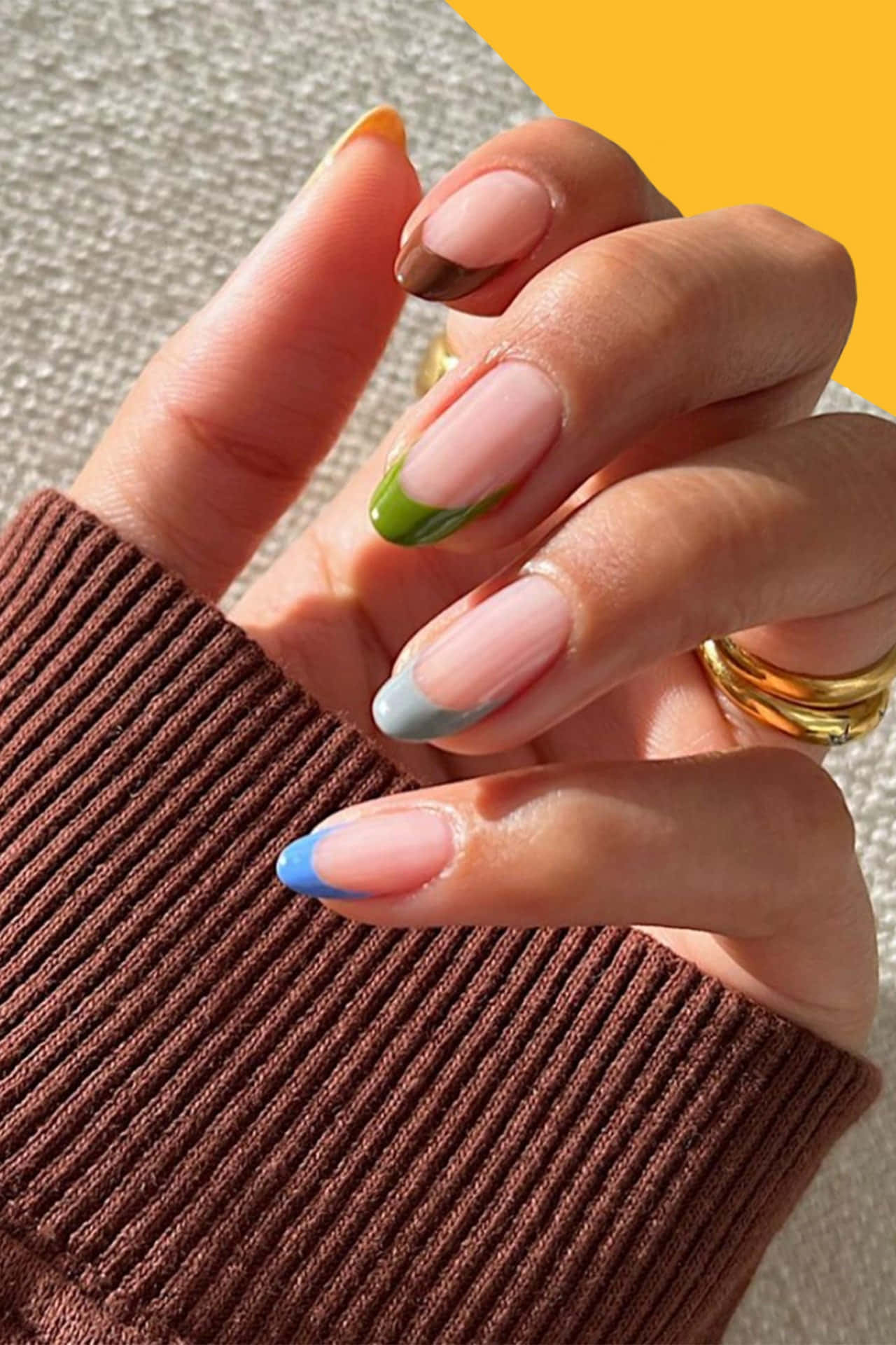 Fake Nail 桌布 壁紙 — 一隻手的特寫，有色彩繽紛的漸變指甲和金戒指，背景是有紋理的棕色毛衣和亮黃色背景。