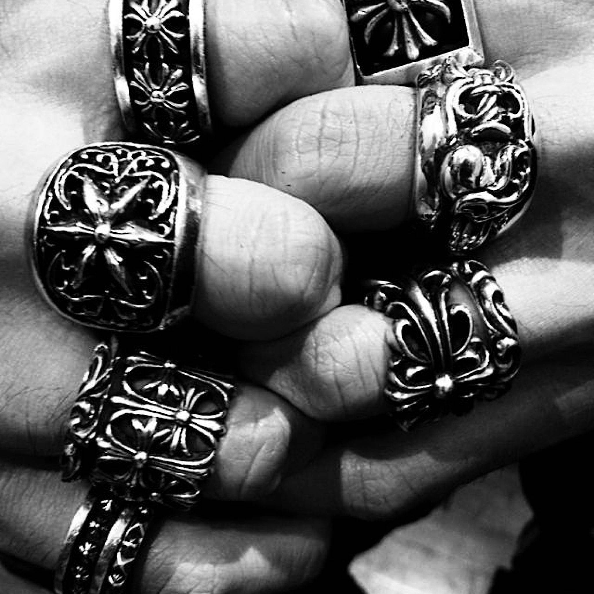 Chrome Hearts 桌布 壁紙 — 一隻手的黑白特寫鏡頭，手上戴著華麗、精緻的戒指，上面有複雜的花卉和幾何圖案。