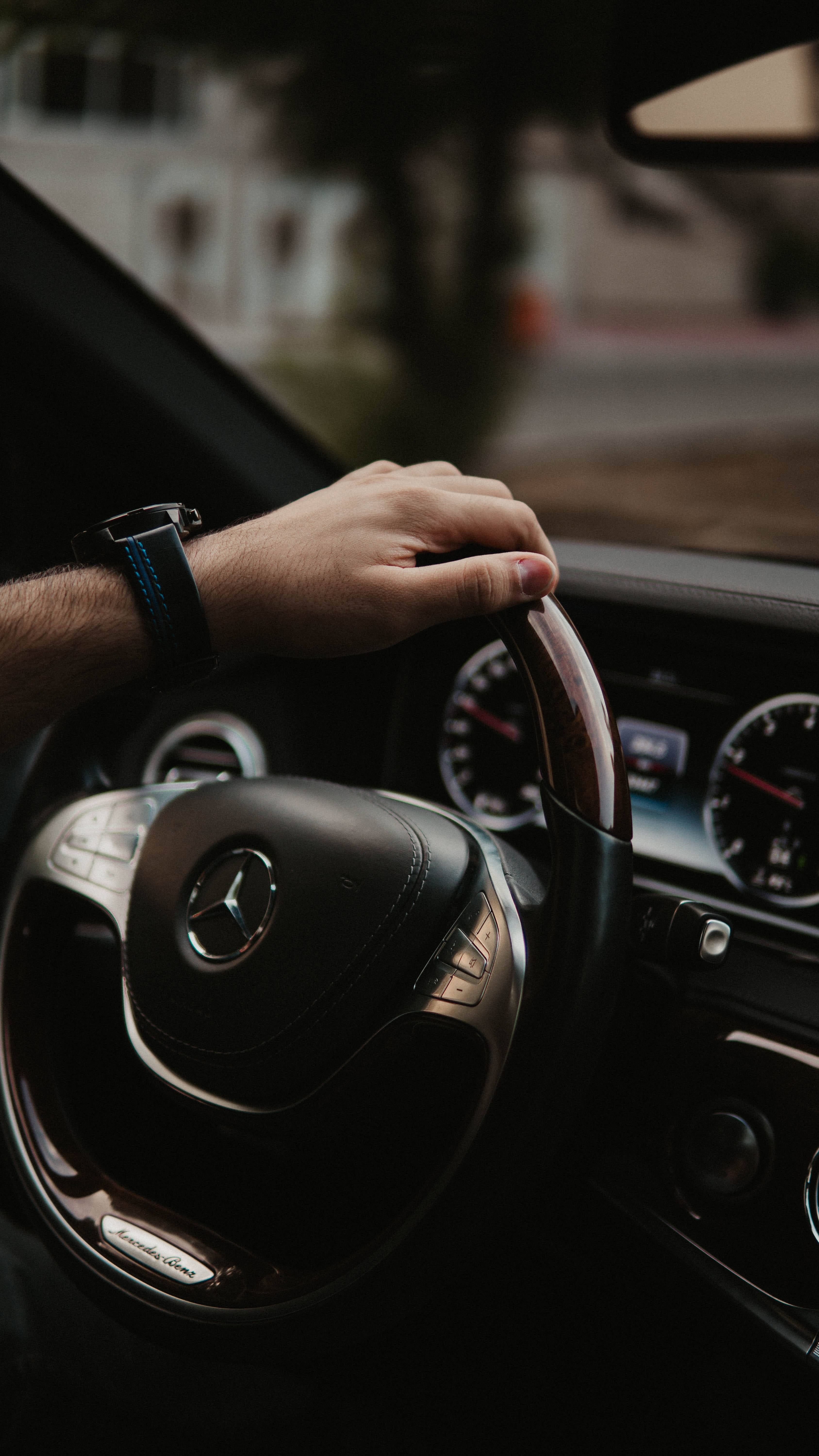跑車 桌布 壁紙 — 一隻手緊握車內時尚黑色Mercedes-Benz方向盤的特寫，周圍是模糊的城市環境。