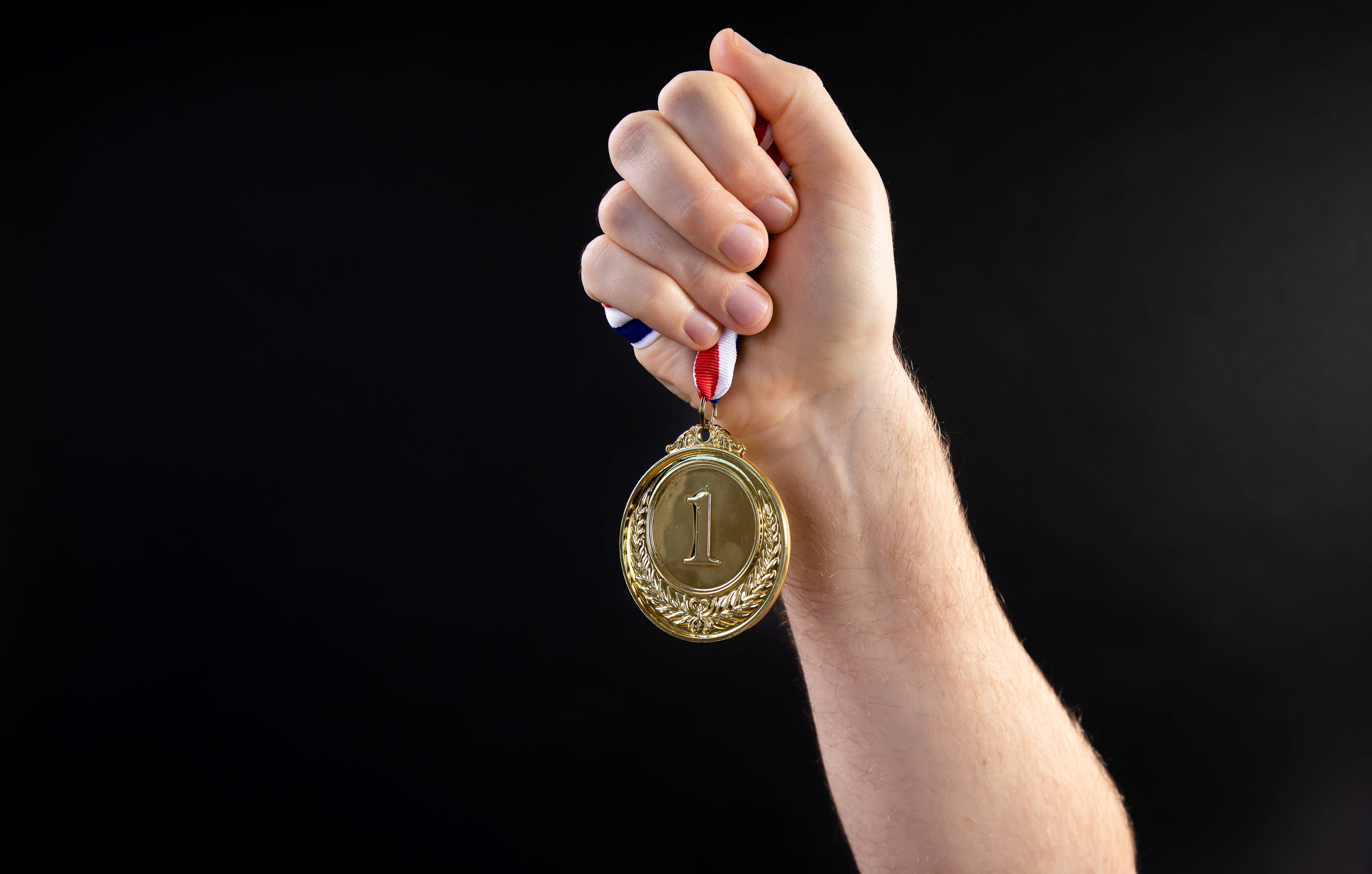 Victory 桌布 壁紙 — 一隻手自豪地握著一枚金色第一名獎牌，背景是純黑色。