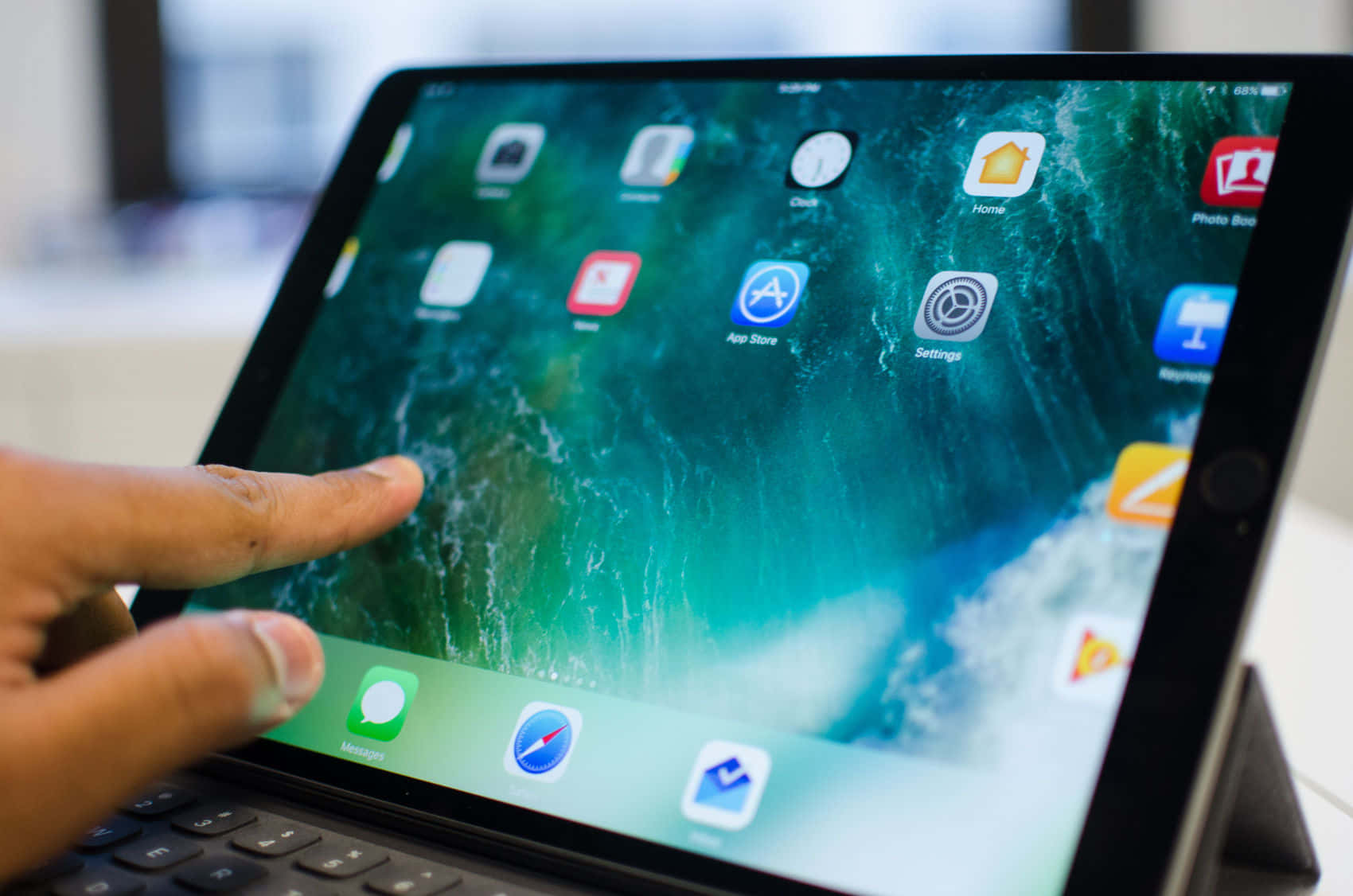 iPad 桌布 壁紙 — 一隻手輕觸iPad螢幕，顯示帶有應用程式圖示的藍綠色海浪桌布。