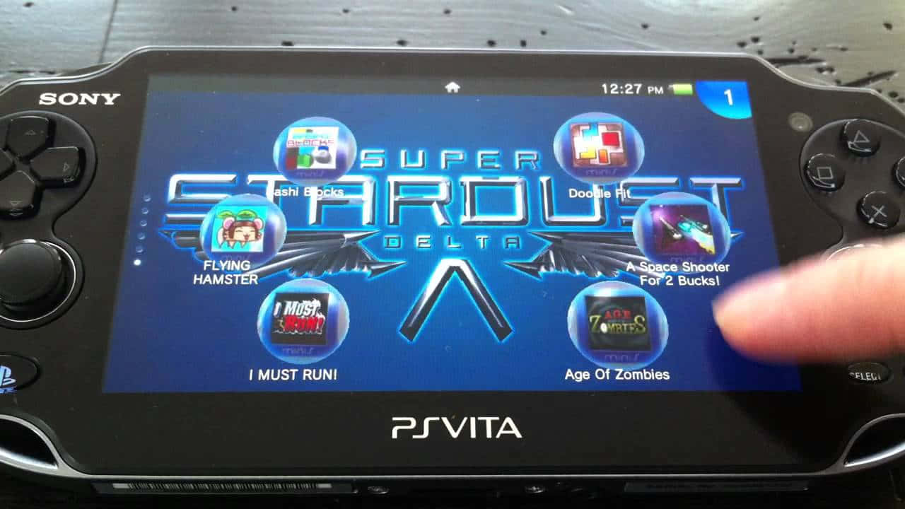Ps Vita 桌布 壁紙 — 一隻手輕觸PS Vita螢幕，顯示帶有彩色應用程式圖示的Super Stardust Delta遊戲選單。