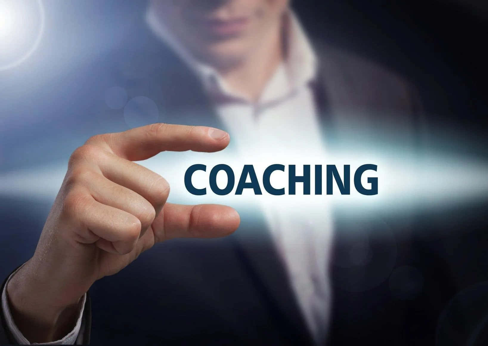 Coach 桌布 壁紙 — 一隻手輕觸一個發光的數位螢幕，上面顯示「coaching」一詞，背景是模糊的商人。