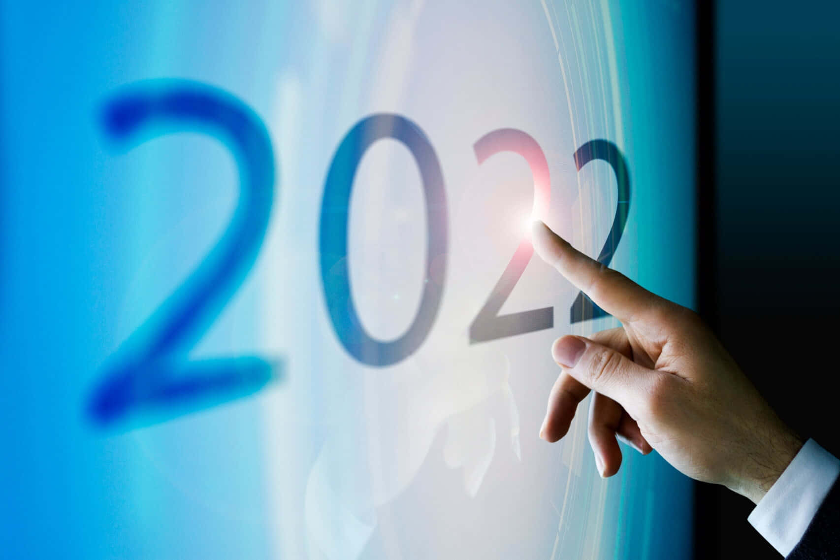 pointing 桌布 壁紙 — 一隻手輕觸一個發光的數位螢幕，顯示2022年，並帶有明亮的光暈。