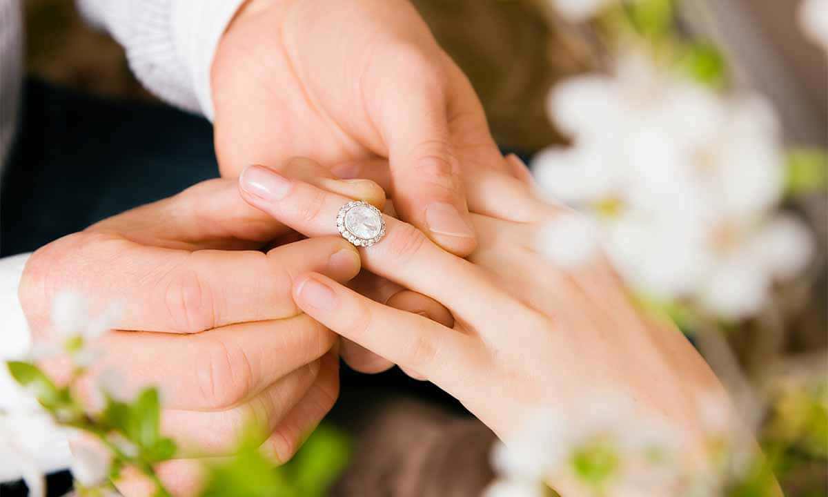 Marriage 桌布 壁紙 — 一隻手輕輕地將閃爍的鑽石訂婚戒指戴在另一人的手指上，周圍是柔軟的白色花朵。