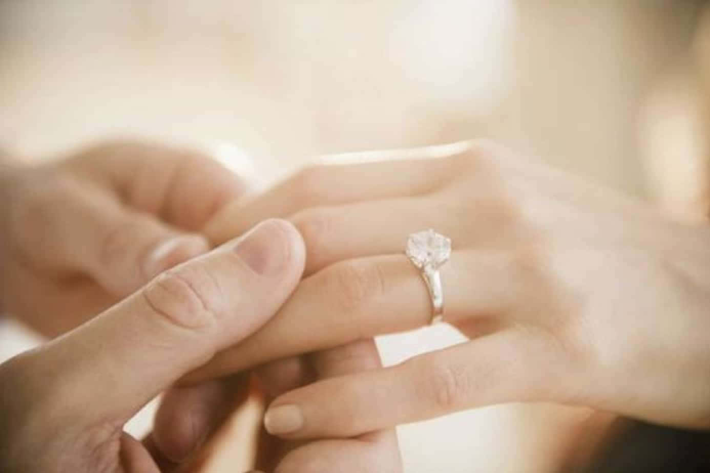 Marriage 桌布 壁紙 — 一隻手輕輕地將閃閃發光的鑽石訂婚戒指戴在另一隻手上，背景柔和模糊。