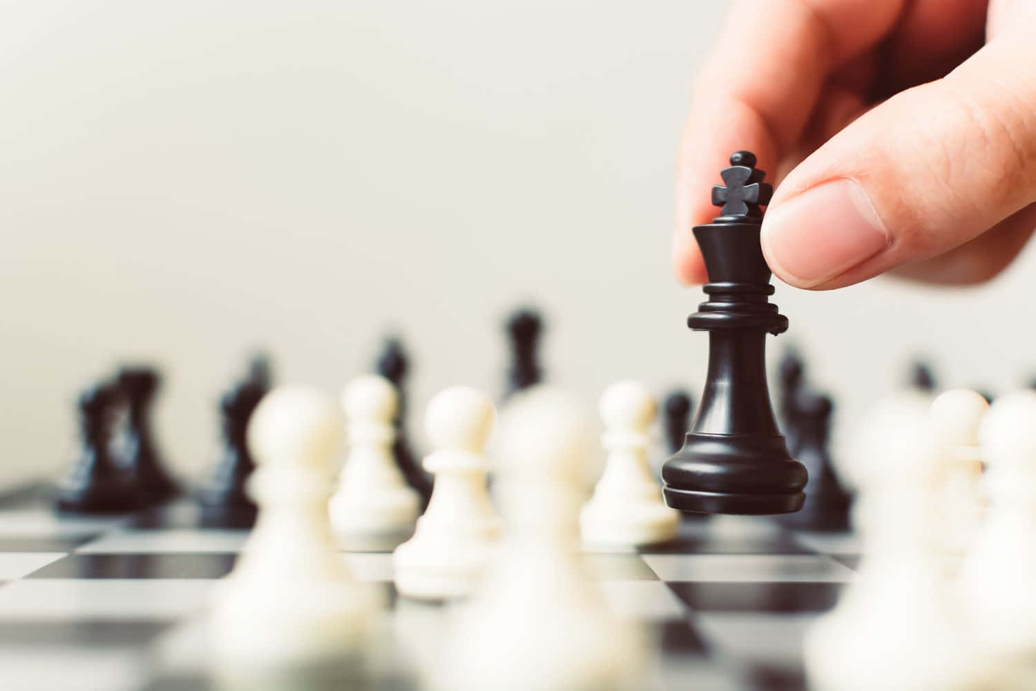 Black And White Chess 桌布 壁紙 — 一隻手輕輕地將黑色西洋棋國王舉起在模糊的棋盤上方，對手的棋子處於柔焦狀態。