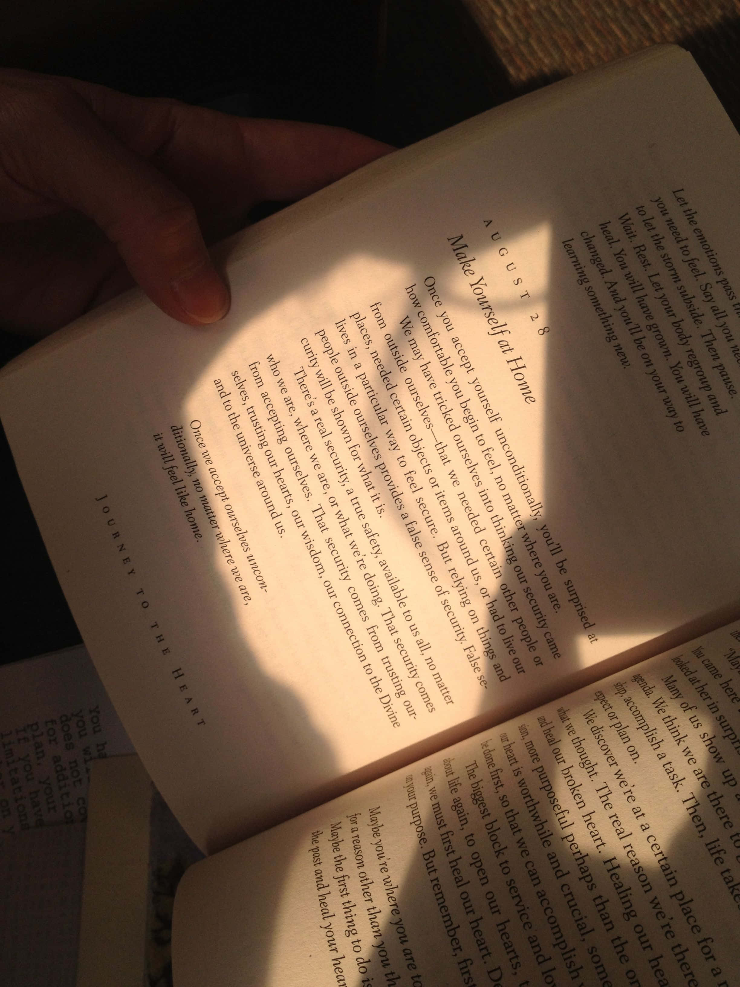 Open Book 桌布 壁紙 — 一隻手輕輕托住一本打開的書，書名為「Make Yourself at Home」，溫暖的陽光在書頁上投下柔和的光輝。