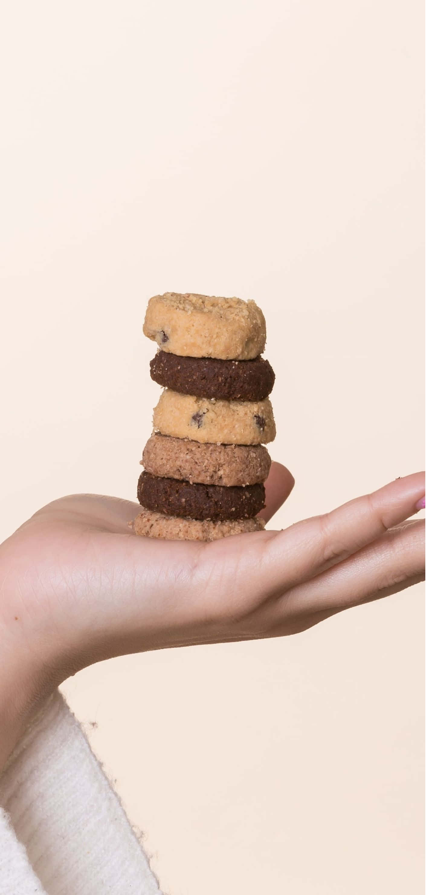 Cookies 桌布 壁紙 — 一隻手輕輕拿著一堆五塊不同質感的餅乾，背景是柔和的米色。