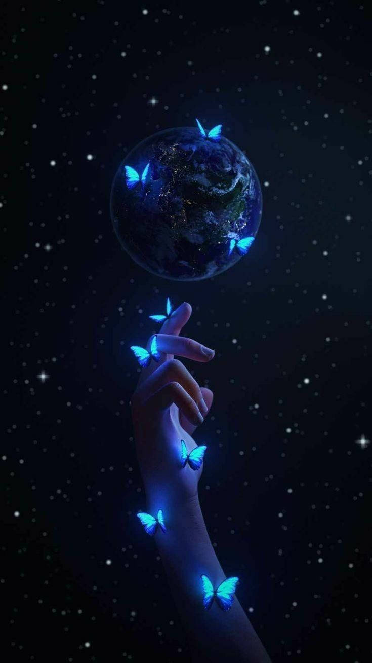 外太空 桌布 壁紙 — 一隻手輕輕捧著一個發光的藍色地球，周圍環繞著發光的蝴蝶，背景是繁星點點的夜空。
