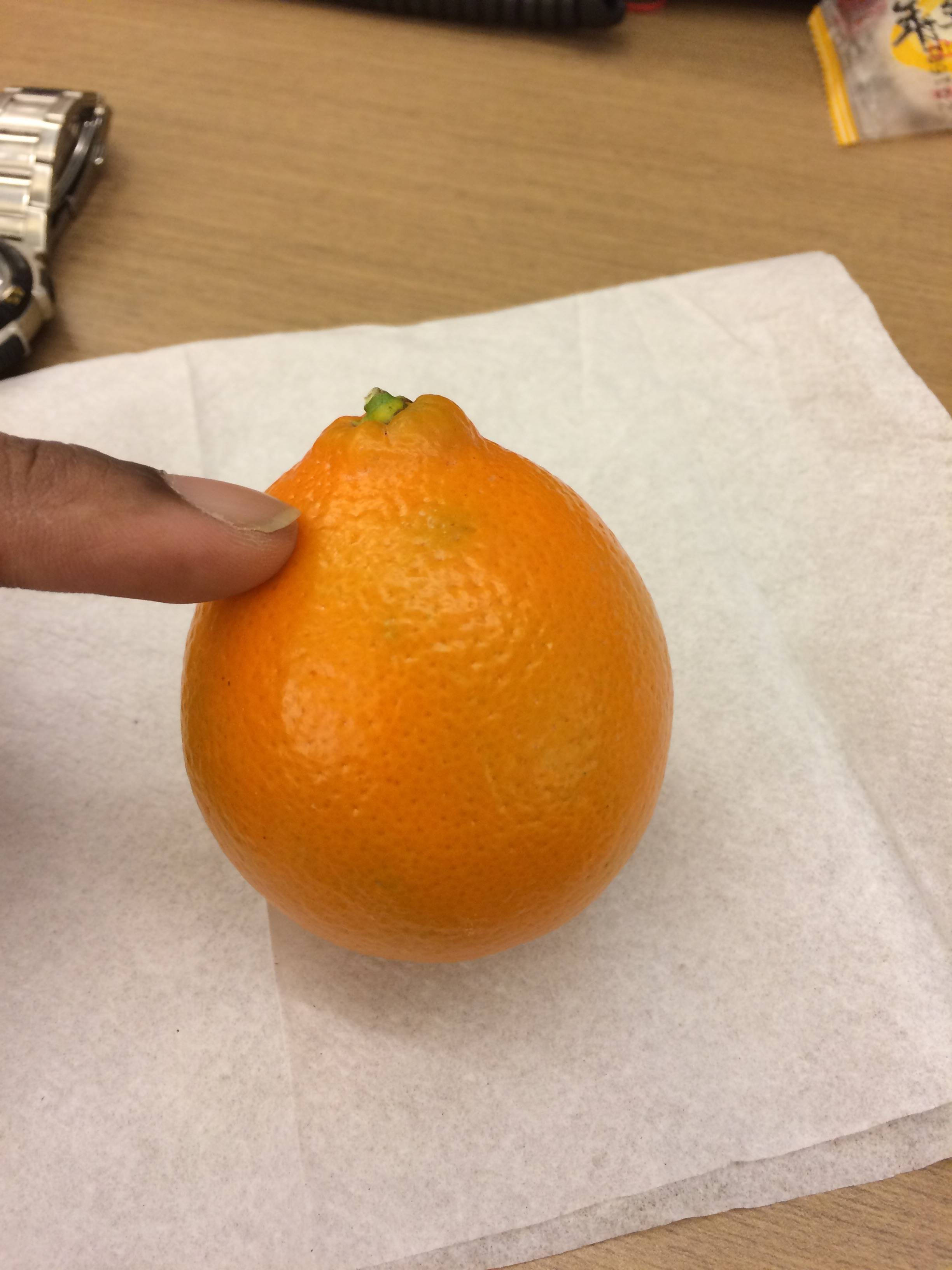 Fruit 桌布 壁紙 — 一隻手輕輕握住一個放在木桌上白色紙巾上的亮橙色柑橘類水果。