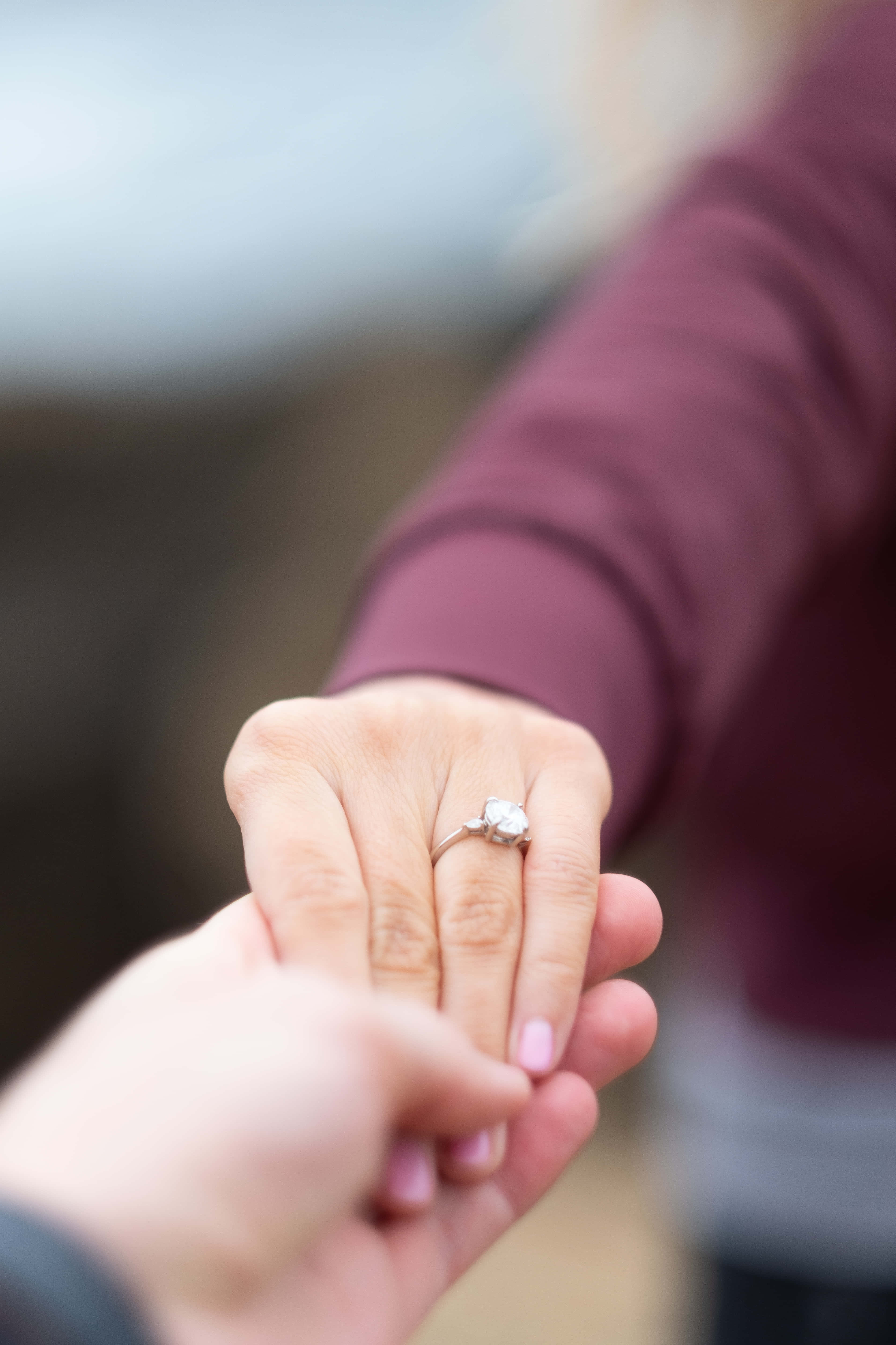 Holding Hands 桌布 壁紙 — 一隻手輕輕握住另一隻戴著閃亮鑽石訂婚戒指的手的特寫。