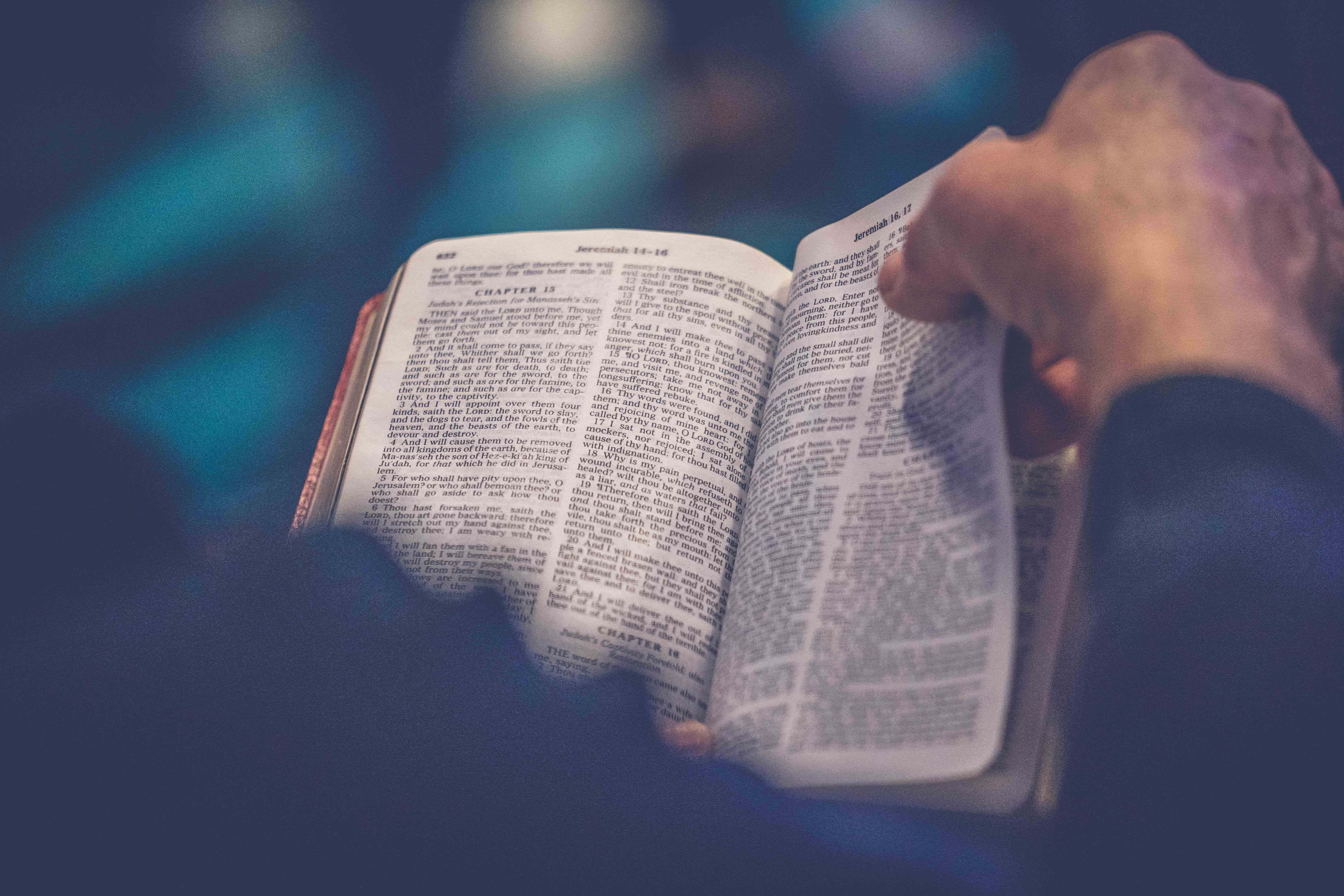 Gospel 桌布 壁紙 — 一隻手輕輕握著一本打開的聖經，可見章節文字，背景為柔和藍色。