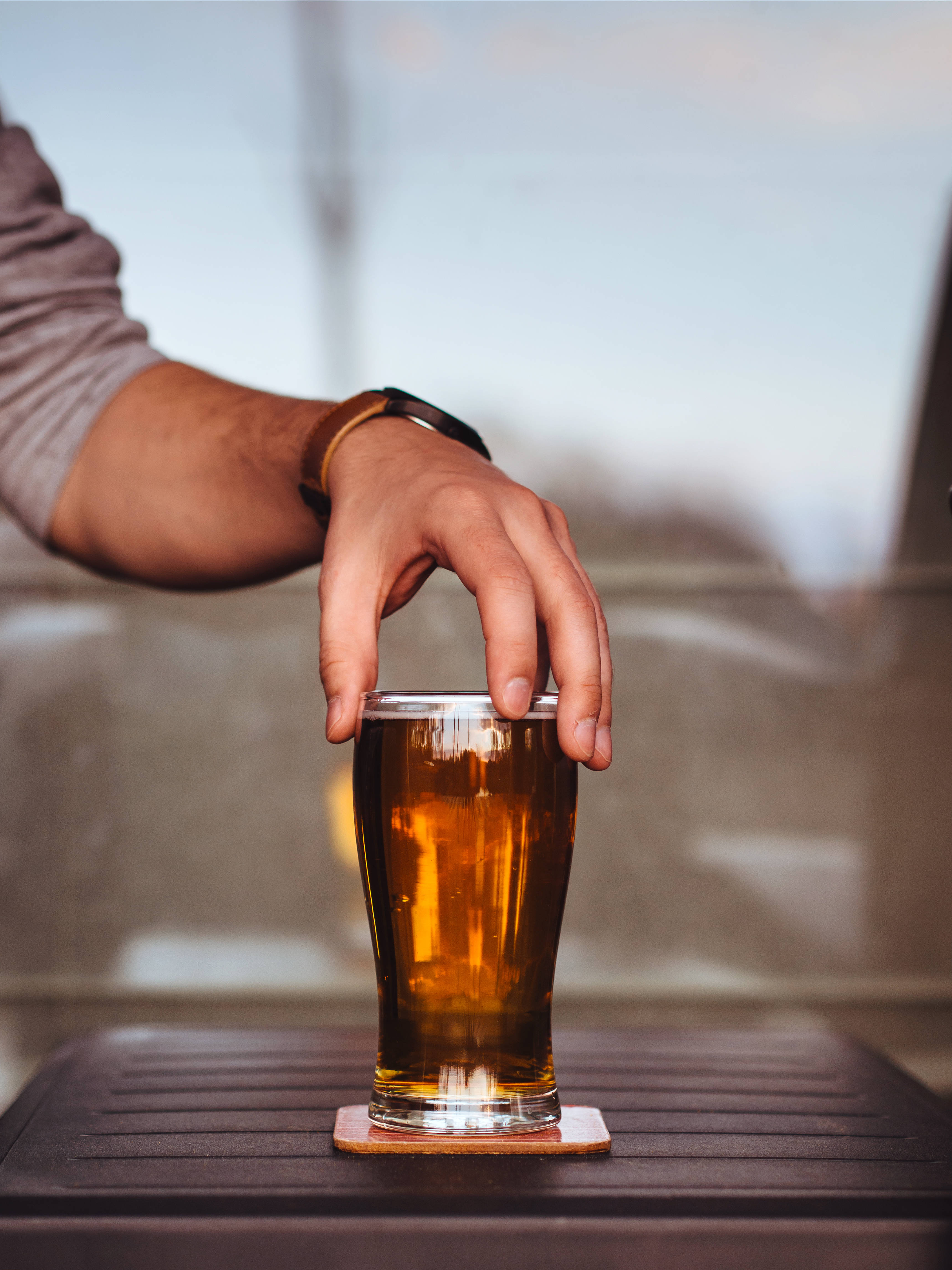 beer chug 桌布 壁紙 — 一隻手輕輕放在木桌上杯墊上的琥珀色啤酒杯上。