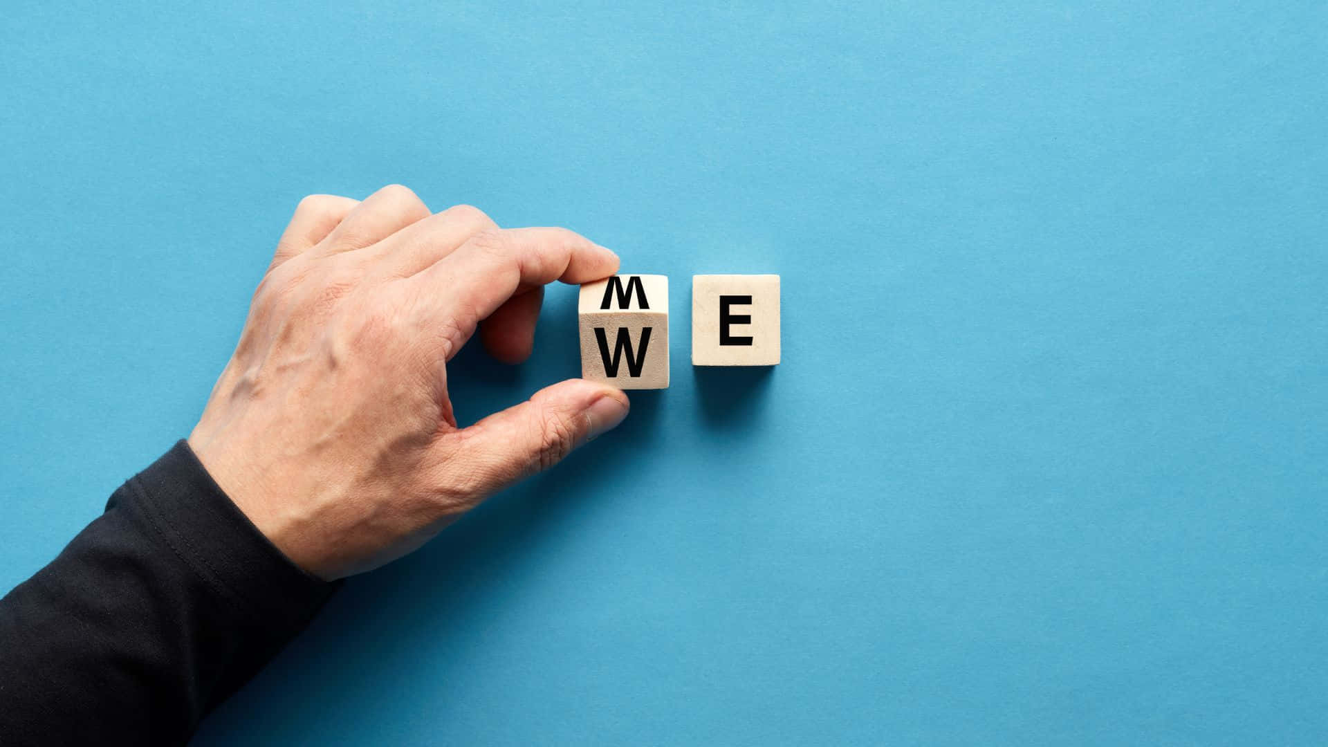 Me 桌布 壁紙 — 一隻手轉動木塊，將「WE」改為「ME」，背景為純藍色。
