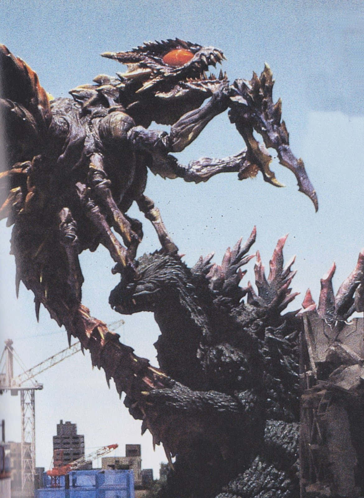Godzilla Vs Megaguirus 桌布 壁紙 — 一隻擁有尖刺肢體和發光橙色眼睛的怪獸卡伊獸，聳立於有建築起重機和建築物的城市景觀之上。