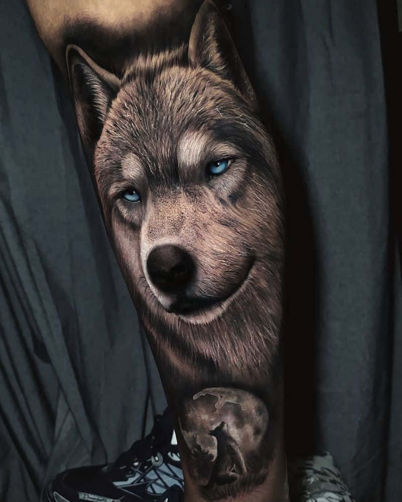Beautiful Wolf 桌布 壁紙 — 一隻擁有銳利藍眼睛和細緻毛髮的狼的超寫實刺青，覆蓋了一個人的前臂和手腕。