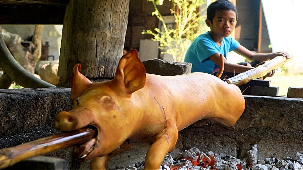 Pig 桌布 壁紙 — 一隻整隻烤豬在熾熱的炭火上轉動，一個小男孩在鄉村戶外環境中專注地觀看。