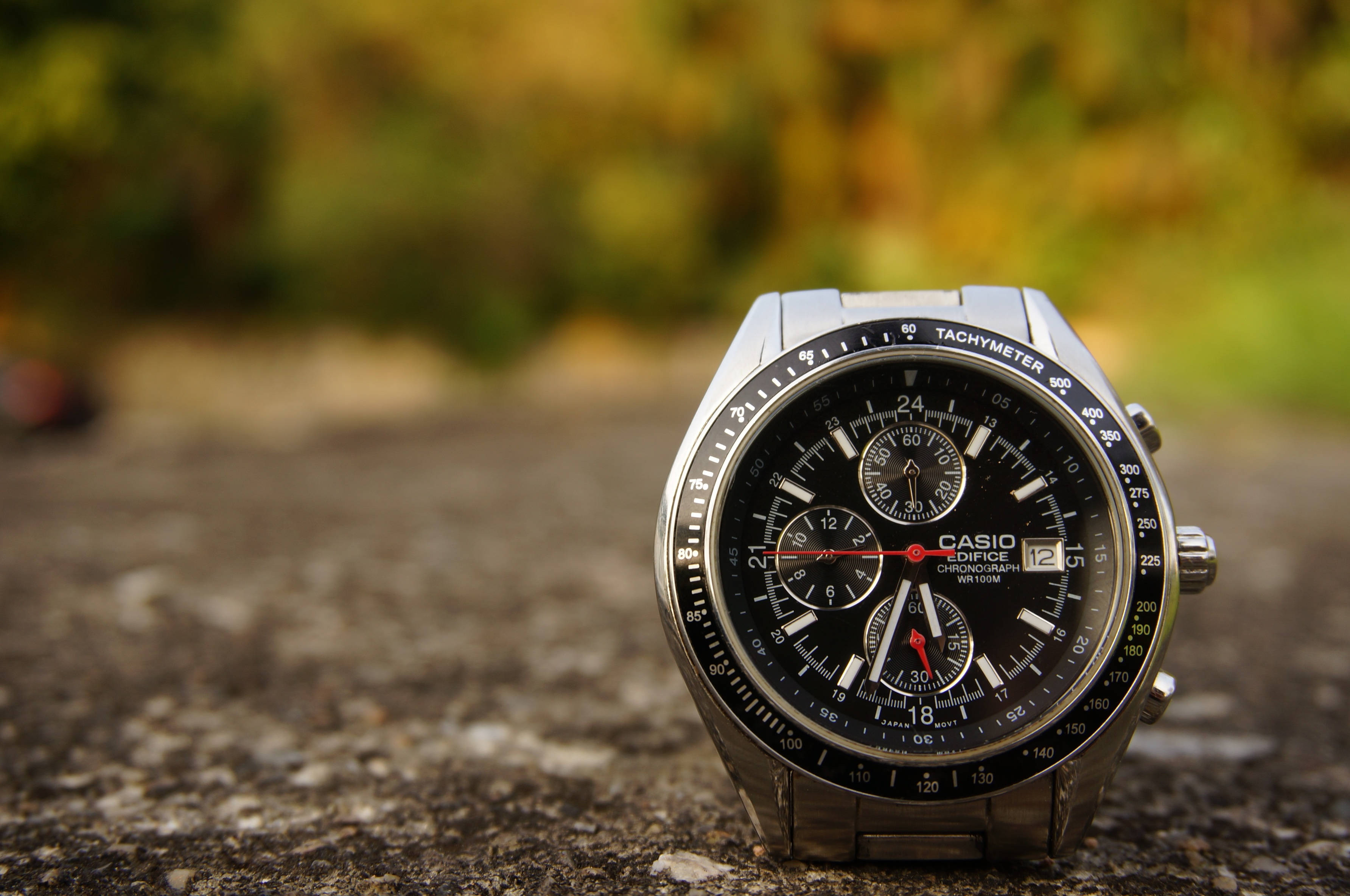 手錶 桌布 壁紙 — 一隻時尚的銀色 Casio Edifice 計時碼錶放在有紋理的石面上，背景是模糊的秋葉。