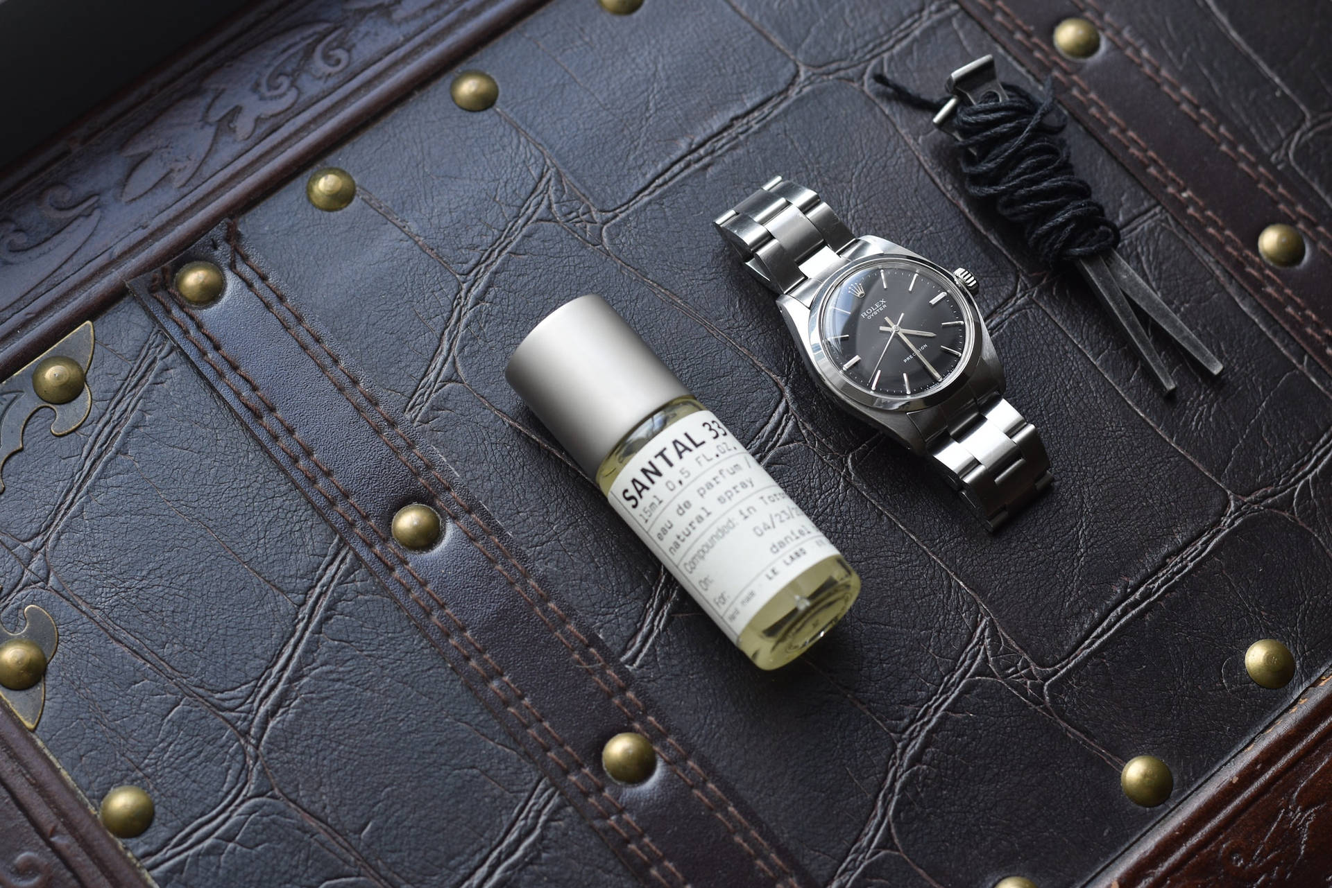 Silver 桌布 壁紙 — 一隻時尚的銀色手錶和一瓶 Santal 33 香水放在帶有黃銅鉚釘的紋理深棕色皮革表面上。