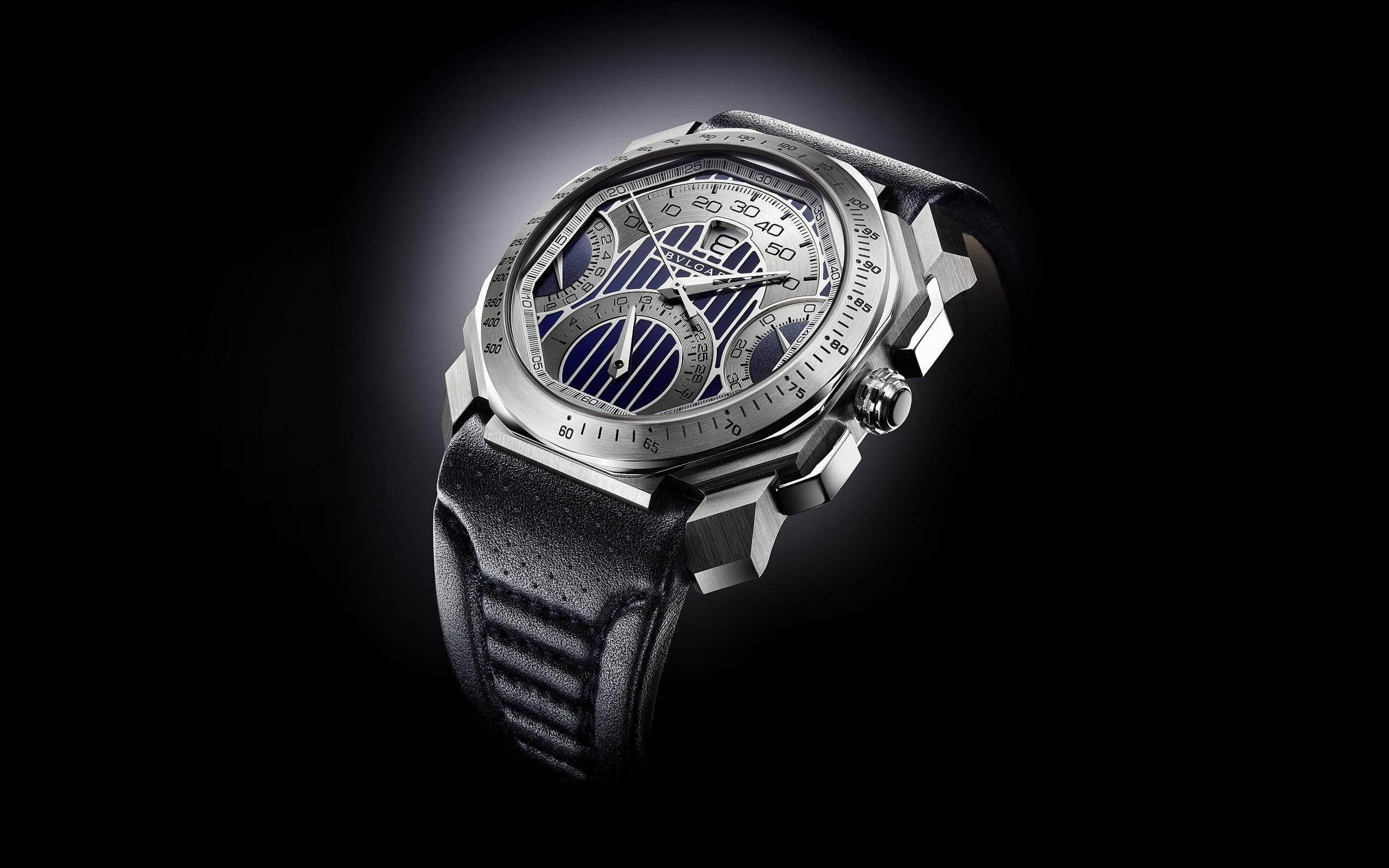Bvlgari 桌布 壁紙 — 一隻時尚的銀色計時碼錶，配備藍色條紋錶盤和黑色皮革錶帶，在深色背景下閃耀光芒。