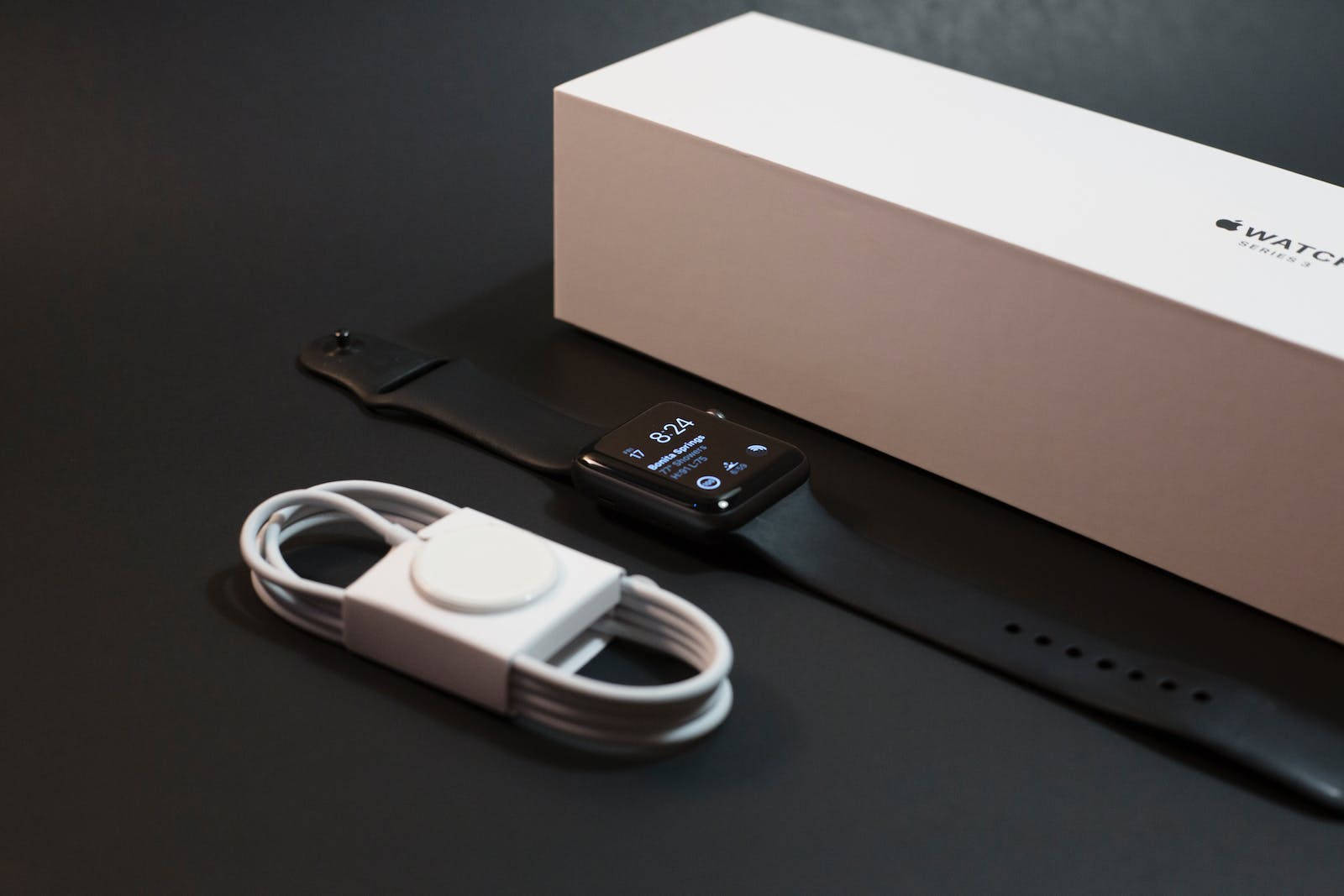黑色Apple Watch Series 3連充電線及盒子在深色表面上。 — 智慧手錶 GIF 壁紙