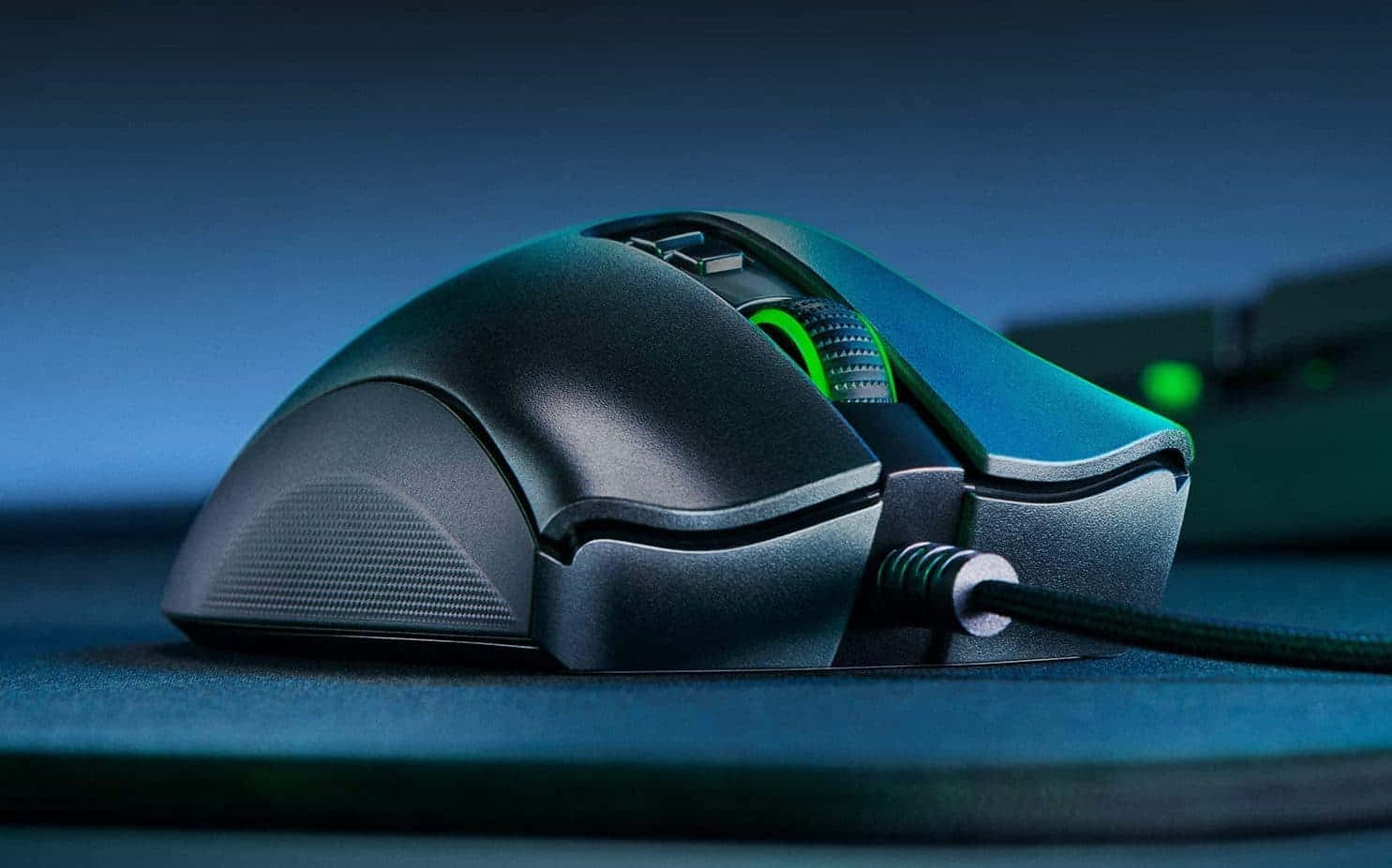 Gaming Mice 桌布 壁紙 — 一隻時尚的黑色電競滑鼠帶有綠色發光點綴，在憂鬱的藍色燈光下放置在深藍色滑鼠墊上。