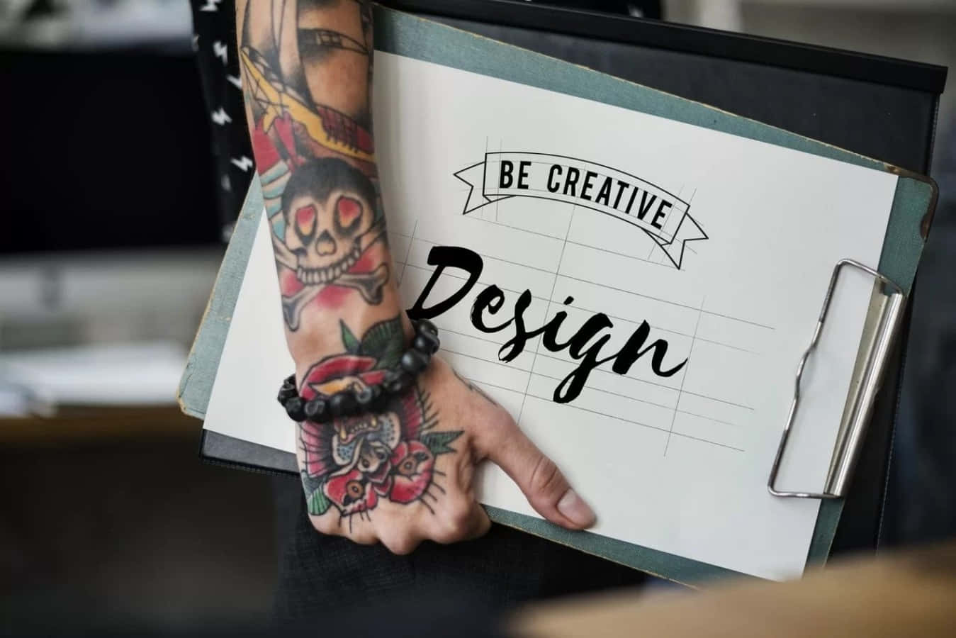graphic design 桌布 壁紙 — 一隻有刺青的手拿著一個寫有「BE CREATIVE Design」的記事板，紙張是方格紙。