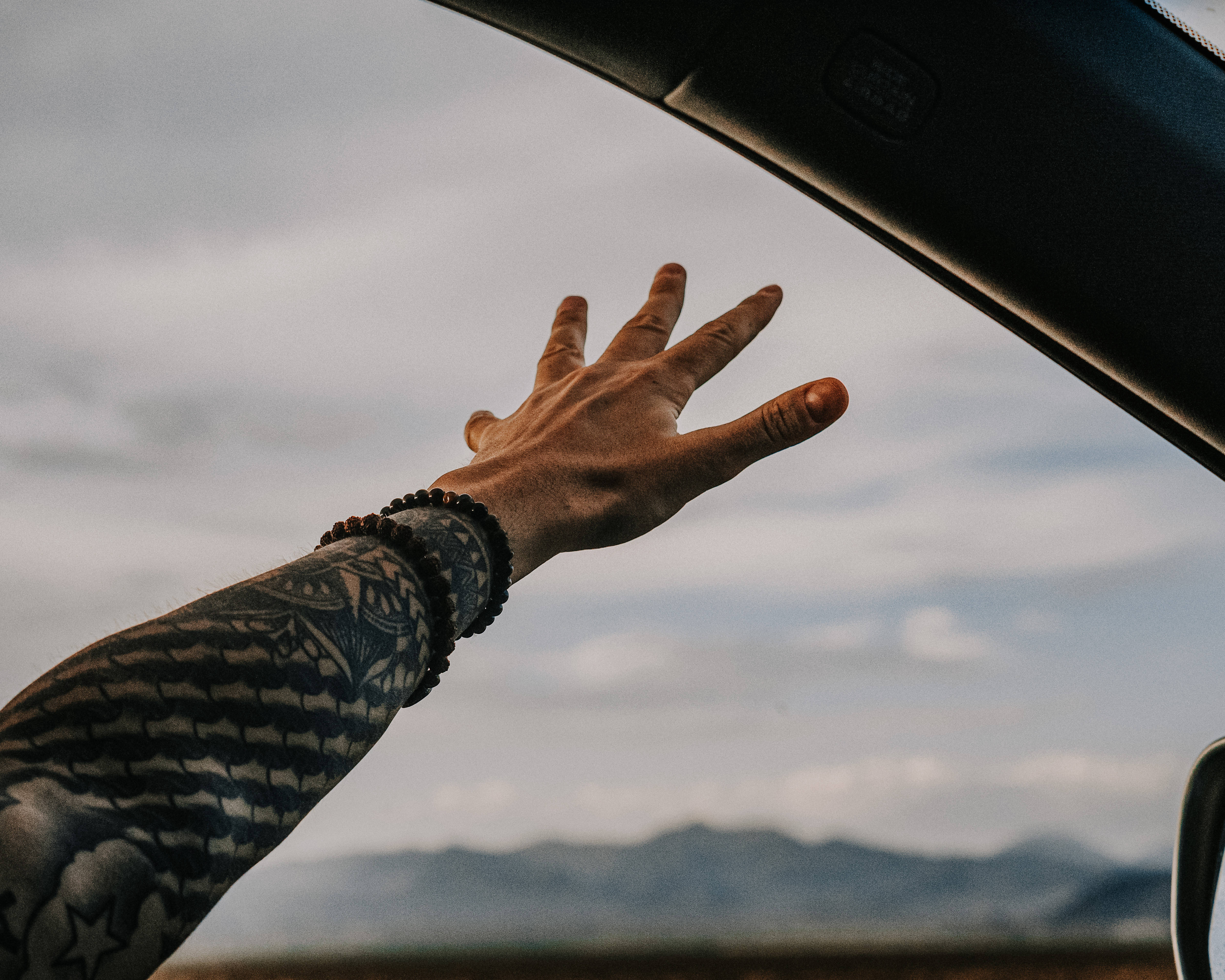 Feels 桌布 壁紙 — 一隻有刺青的手臂從車窗伸出，背景是陰天和遠山。