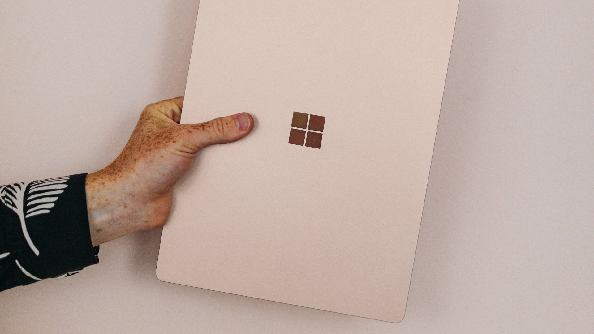 手拿著粉紅色Microsoft Surface筆記型電腦，靠著白色牆壁。