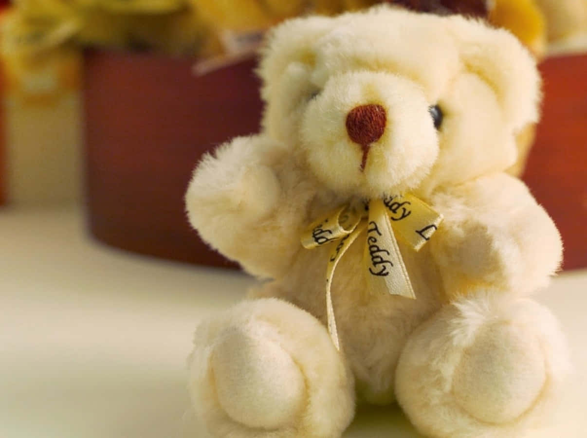Cute Teddy 桌布 壁紙 — 一隻柔軟的奶油色泰迪熊戴著黃色蝴蝶結，溫暖地坐在白色表面上，背景是模糊的花卉。