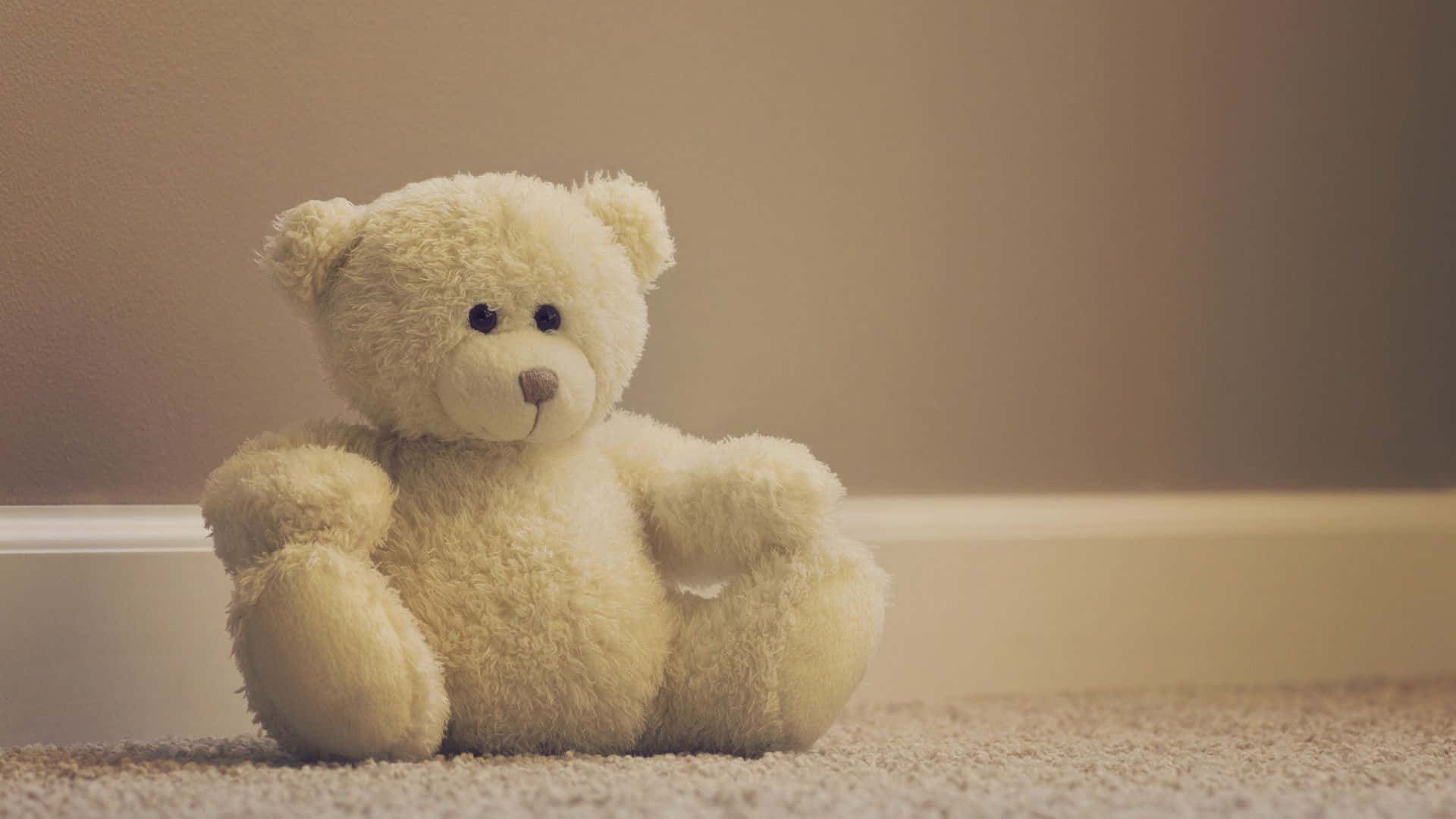 Teddy Bear 桌布 壁紙 — 一隻柔軟的奶油色泰迪熊獨自坐在鋪有地毯的地板上，背景是柔和的米色牆壁。
