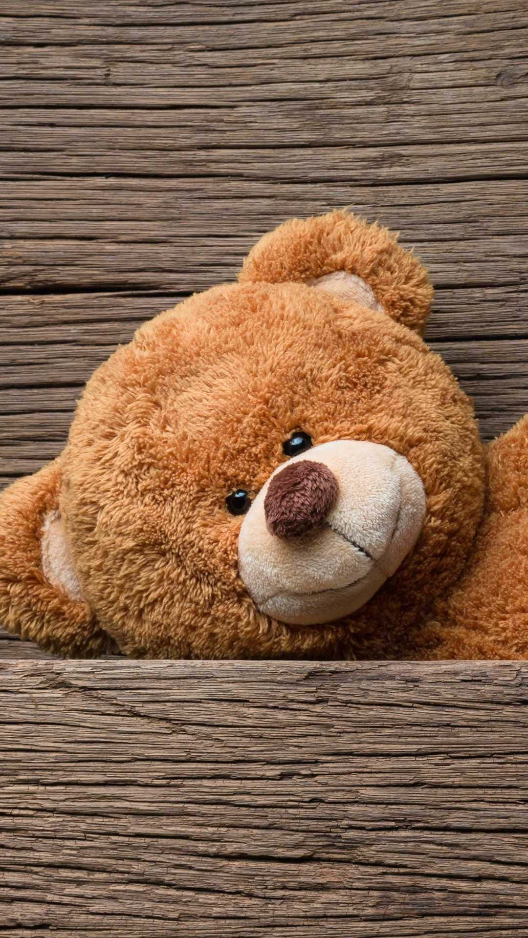 Teddy Bear 桌布 壁紙 — 一隻柔軟的棕色泰迪熊，帶著縫線微笑，將頭靠在風化的木板上。