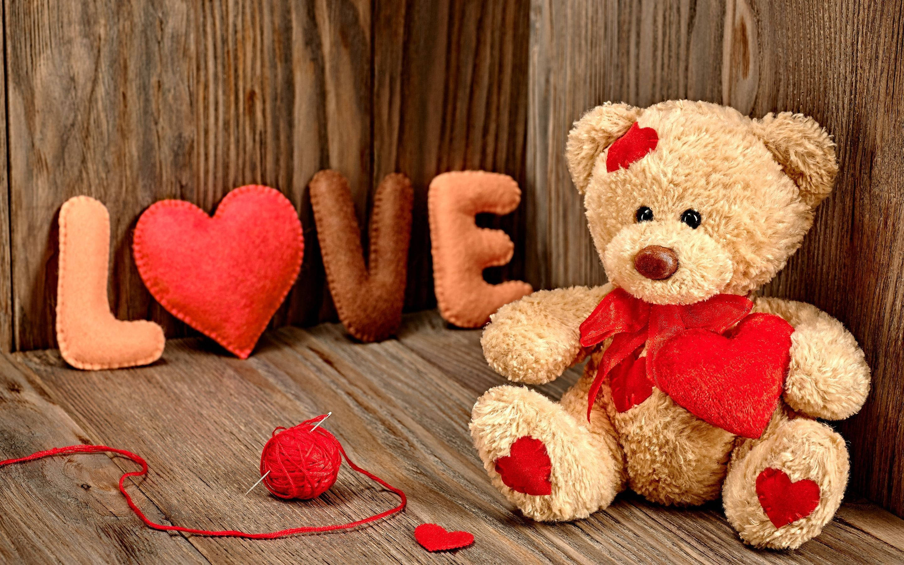 Teddy Bear 桌布 壁紙 — 一隻柔軟的米色泰迪熊帶有紅色心形裝飾，坐在一塊鄉村風格的木質表面上，旁邊是用氈布字母拼成的LOVE。